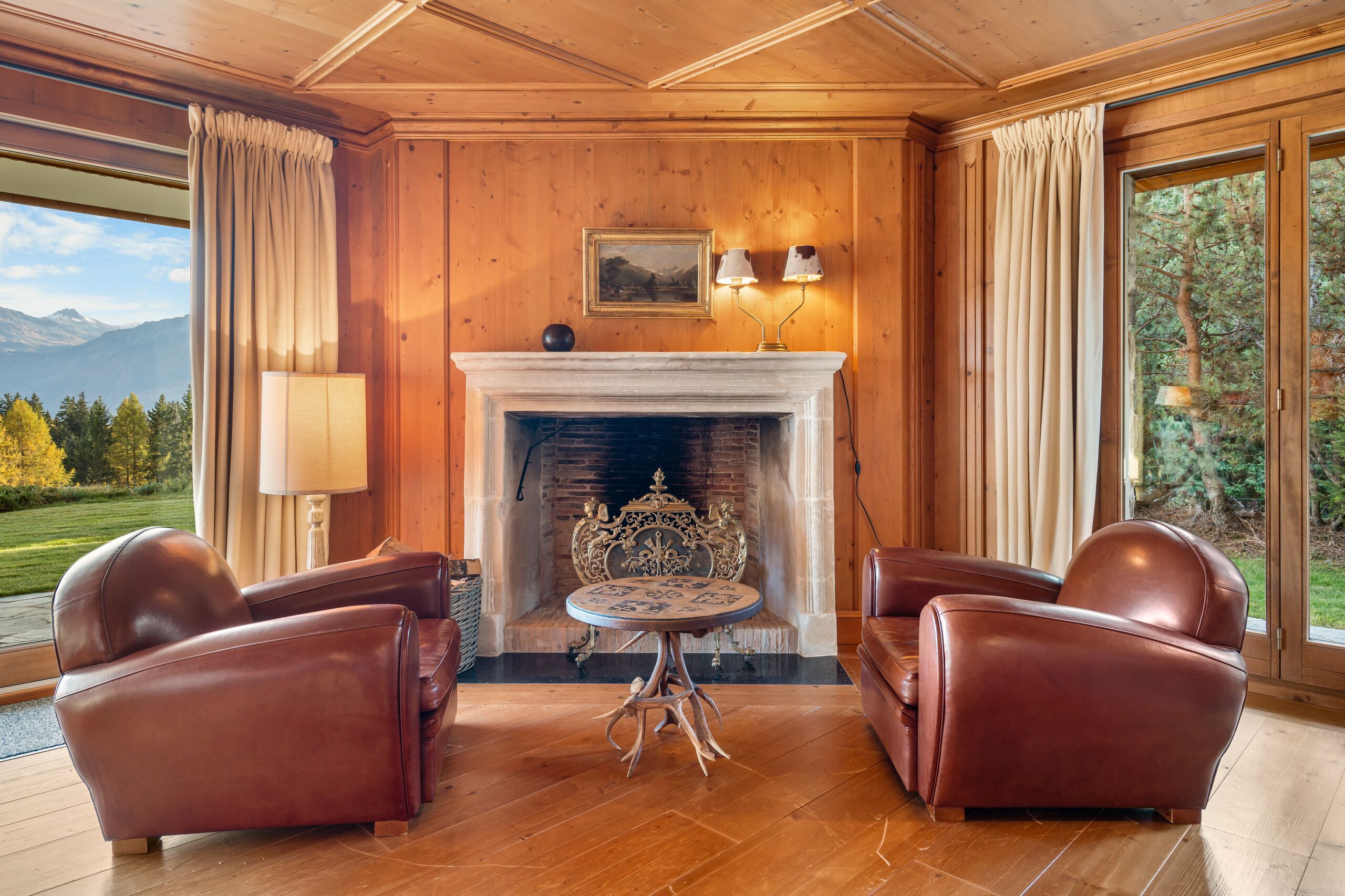 a living room with a fireplace, chairs, and large windows