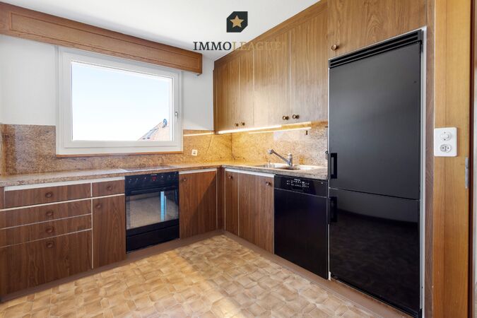 Küche mit Charakter: warme Holzfronten treffen auf moderne Einbaugeräte, dazu ein grosses Fenster mit Ausblick. 