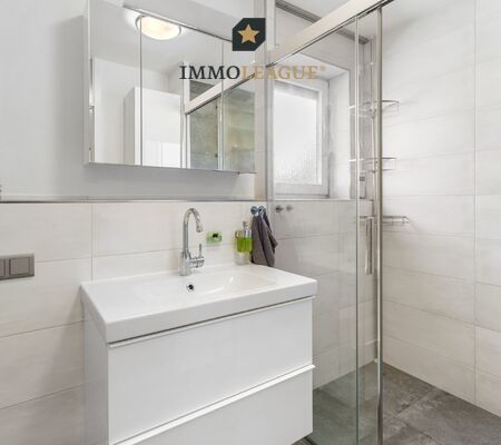 Badezimmer mit klarer Linienführung, begehbarer Dusche mit Sitzfläche für spürbaren Komfort sowie Waschmaschinen- und Trockneranschluss.