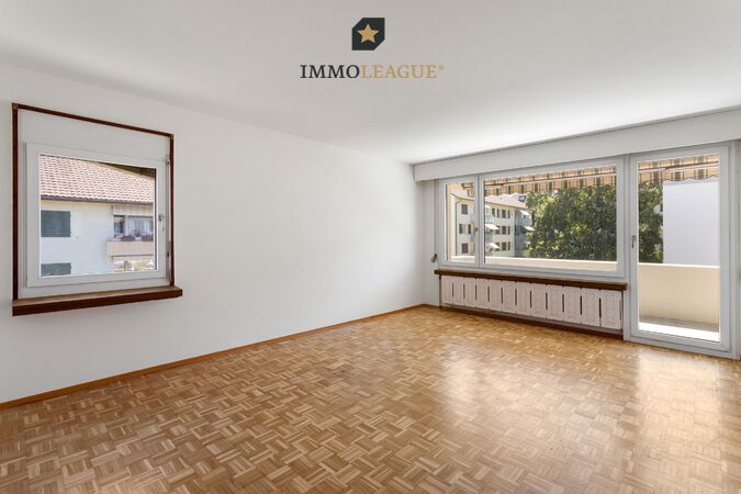 Grosszügiges Wohnzimmer, das mit warmem Parkett und grossen Fenstern viel Licht ins Haus holt und direkten Zugang zum sonnigen Südbalkon bietet.