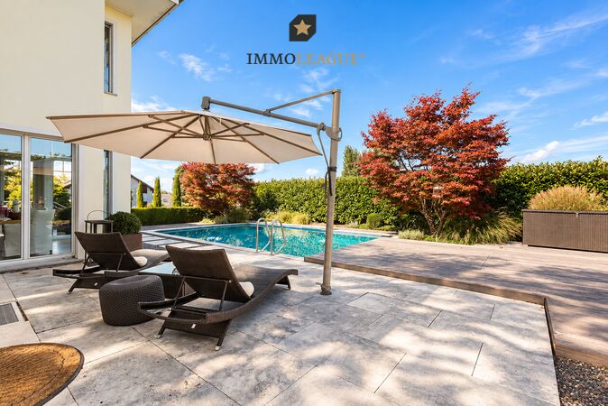 der Garten eines modernen Hauses mit einem großen Swimmingpool und einer Terrasse mit Stühlen und einem Sonnenschirm