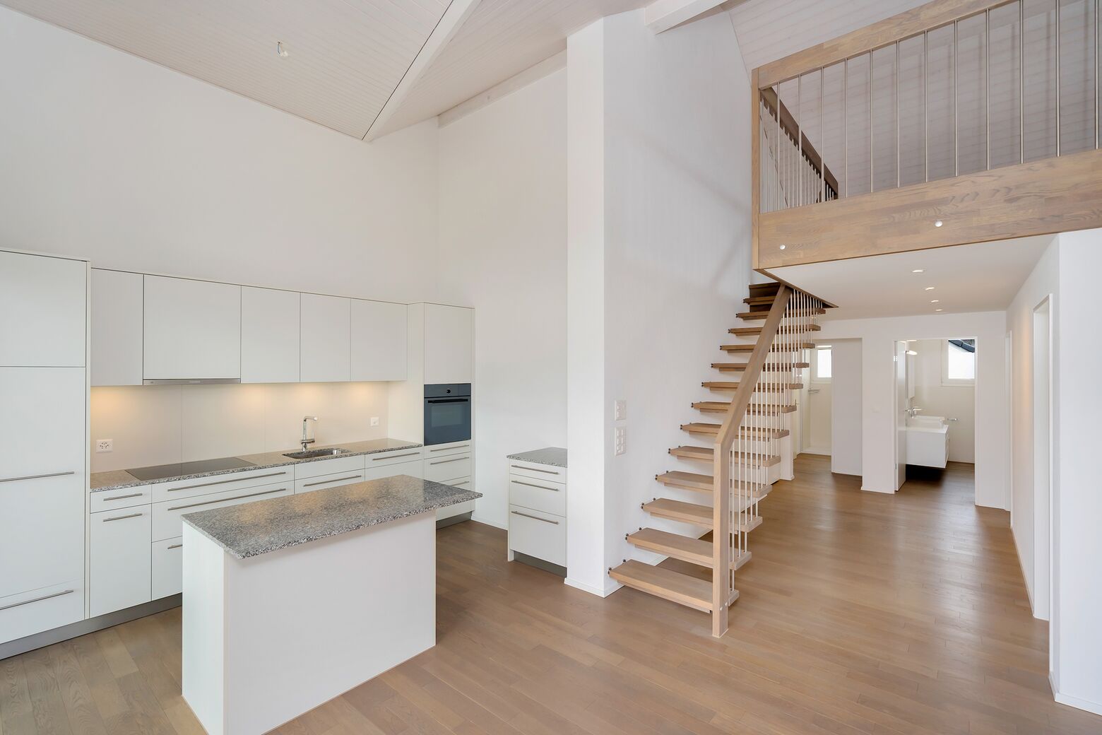 Offene, moderne Küche mit Blick zur massiven Eichenholztreppe zum Galeriegeschoss