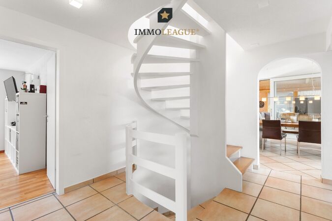 Die geschwungene Wendeltreppe verbindet die Geschosse mit eleganter Linienführung und nimmt die runde Form des Durchgangs zum Essbereich auf.