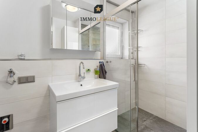 Badezimmer mit klarer Linienführung, begehbarer Dusche mit Sitzfläche für spürbaren Komfort sowie Waschmaschinen- und Trockneranschluss.