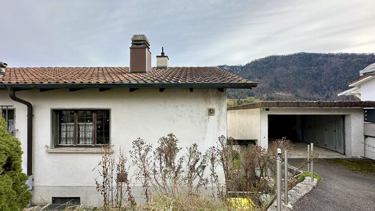 une maison au bord d'une route avec des montagnes en arrière-plan