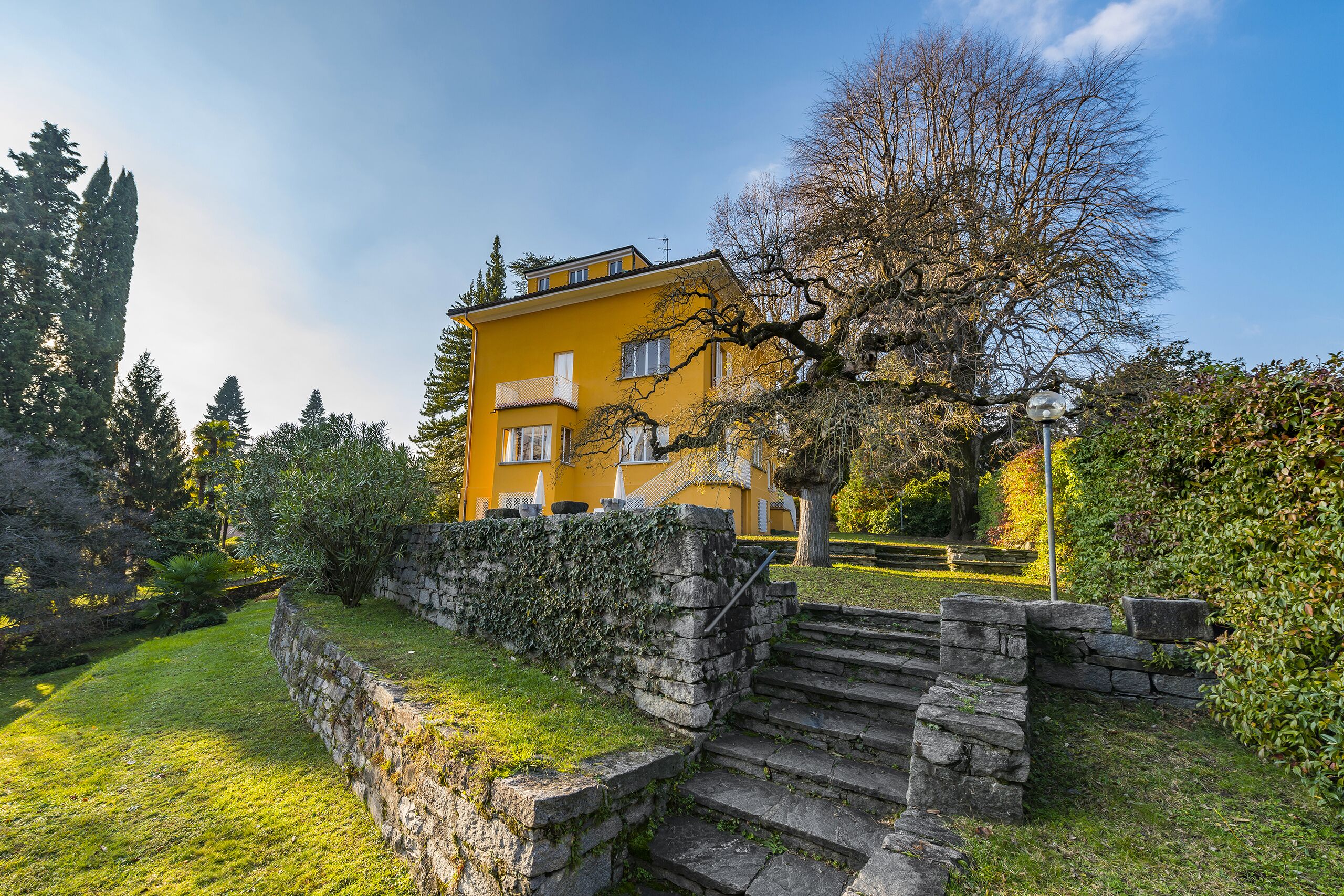 a yellow house with steps and trees in the garden