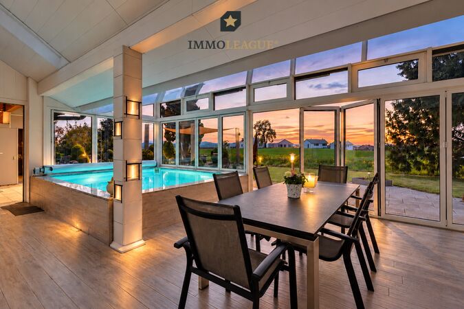 Lichtdurchfluteter Wintergarten mit Indoor-Pool und traumhaftem Blick auf den Sonnenuntergang.