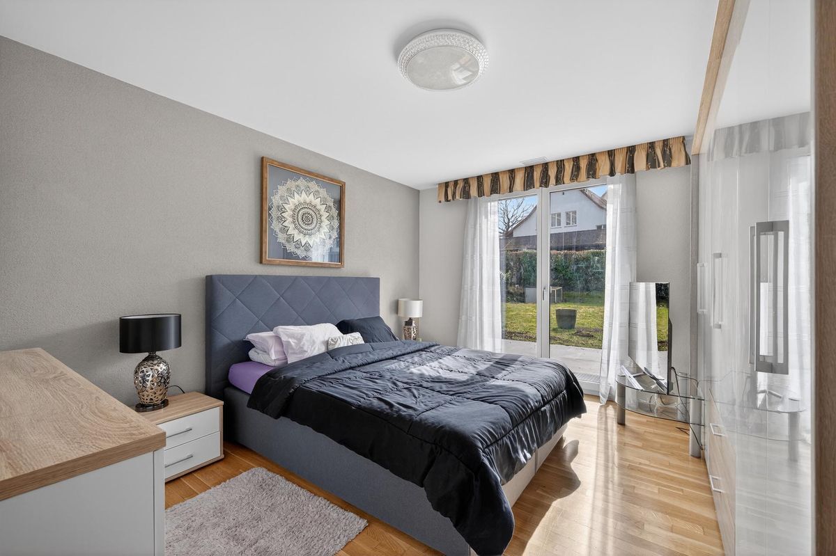 Schlafzimmer mit Zugang zum Garten und grossen Fenstern.