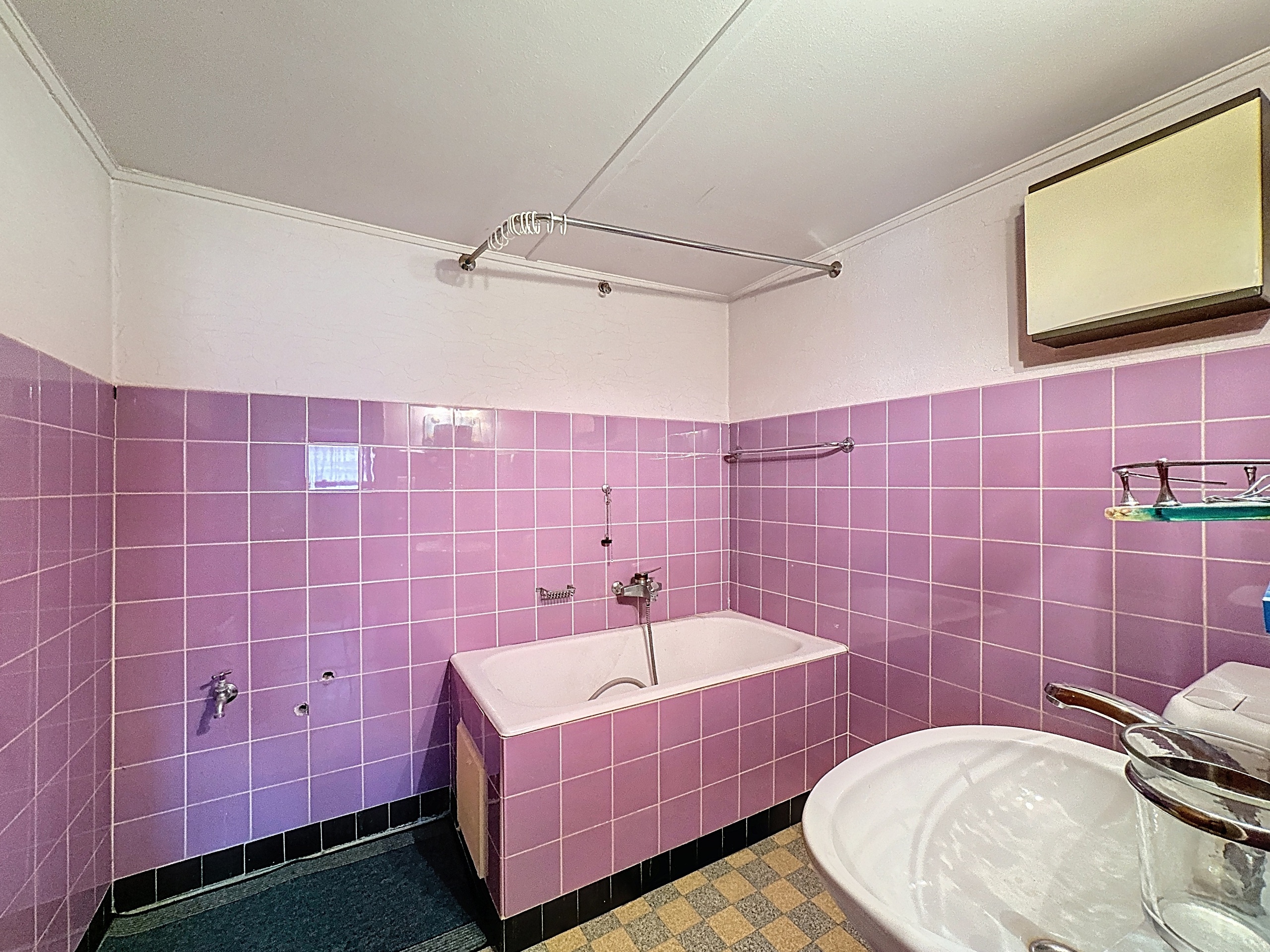 une salle de bains avec des carreaux roses sur les murs et un lavabo, des toilettes et une baignoire blancs