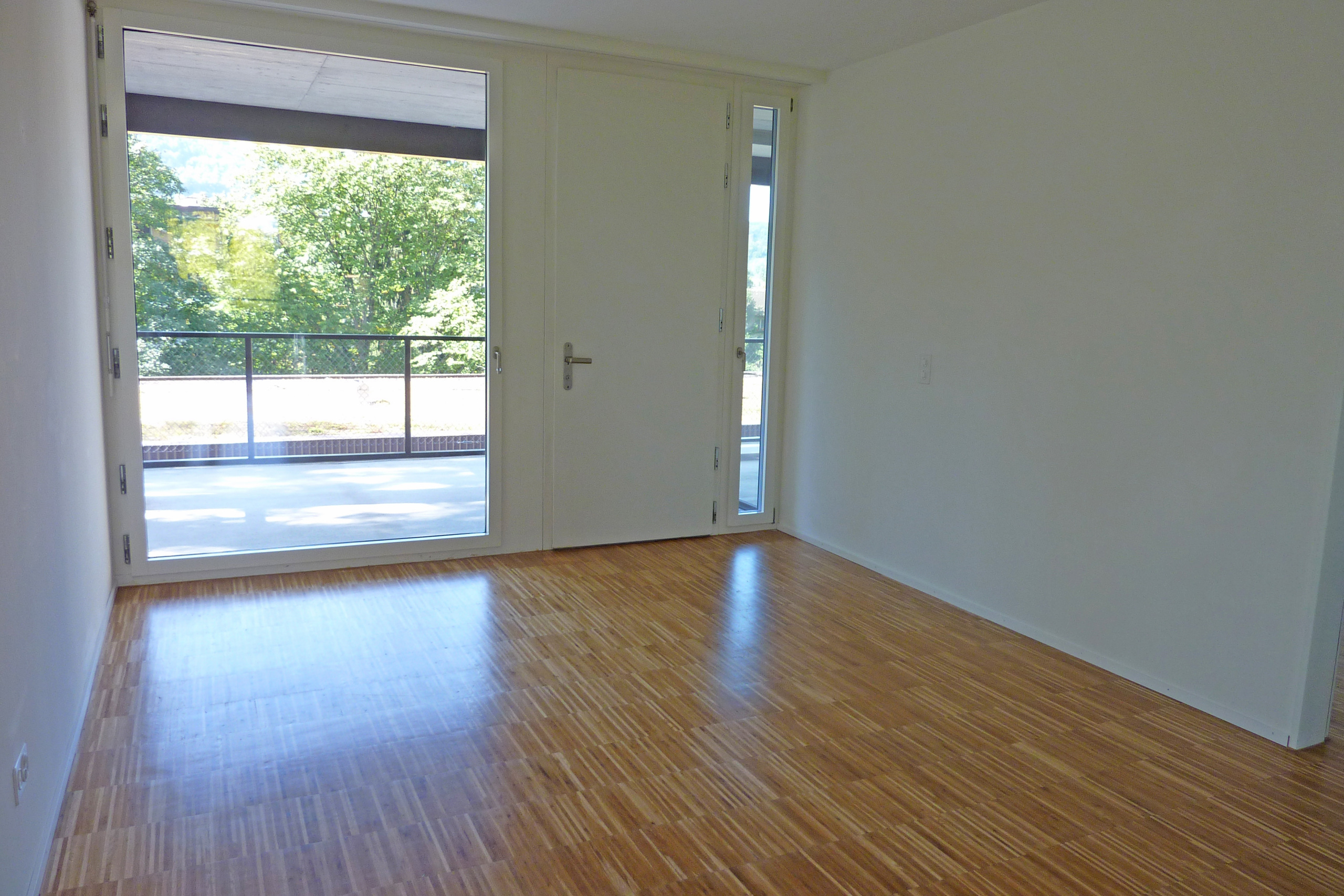 an empty room with wooden floors, a large window, and a sliding glass door that leads into the living room of a house house