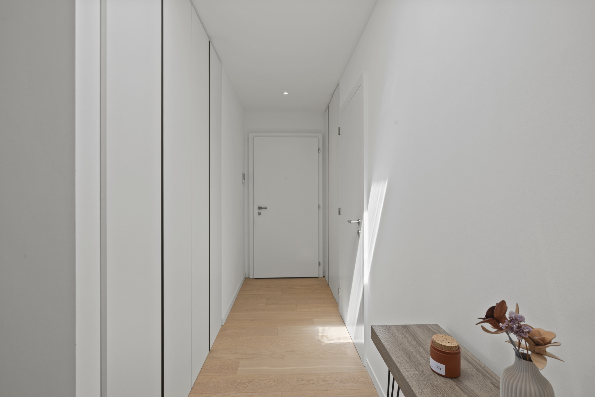 a long hallway with white walls and wooden floor and a long wooden bench at the end of the corridor a long hallway with white walls and wooden floor and a long wooden bench at the end of the corridor