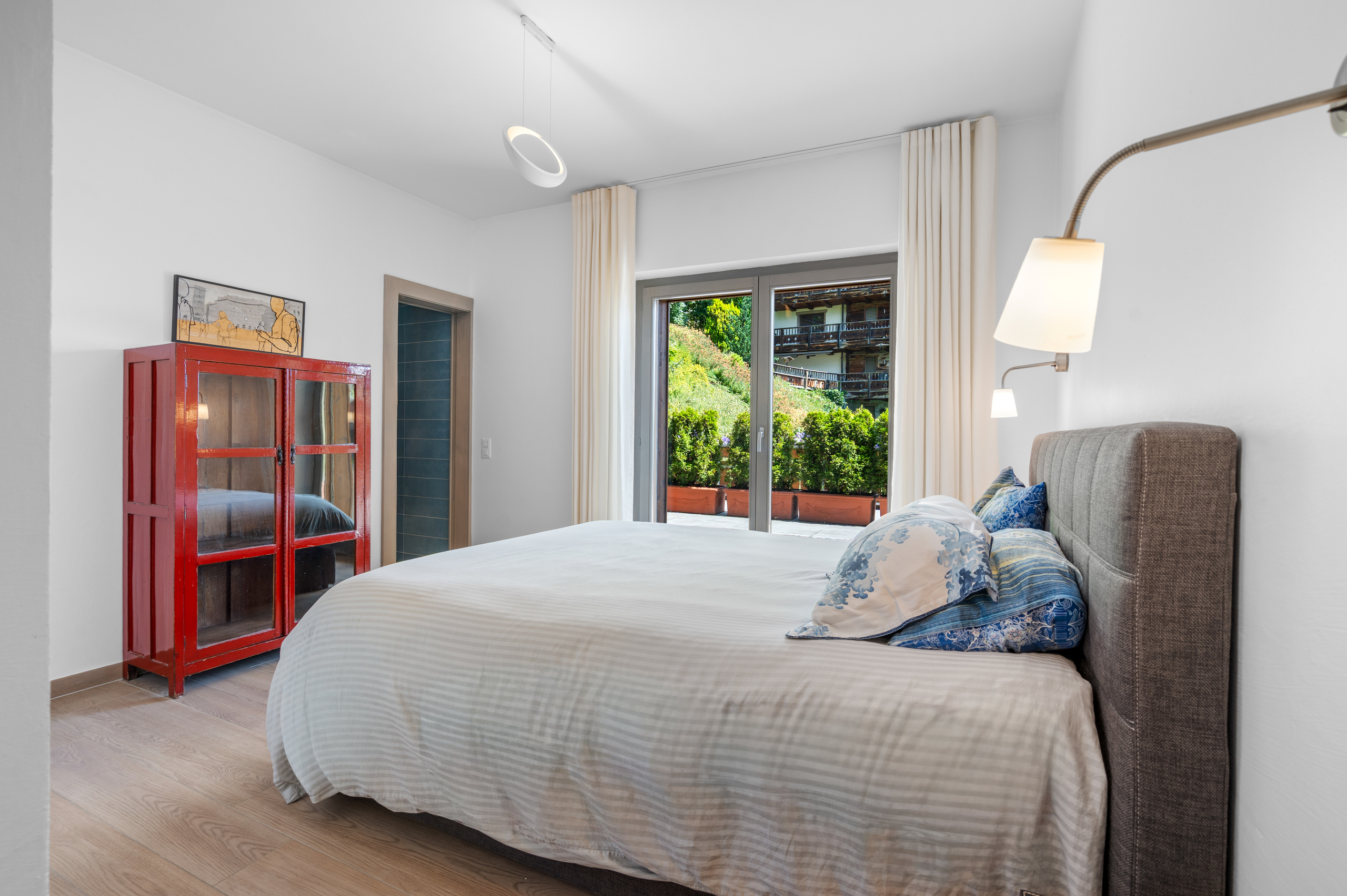 une chambre avec une grande fenêtre, une armoire rouge et un lit blanc