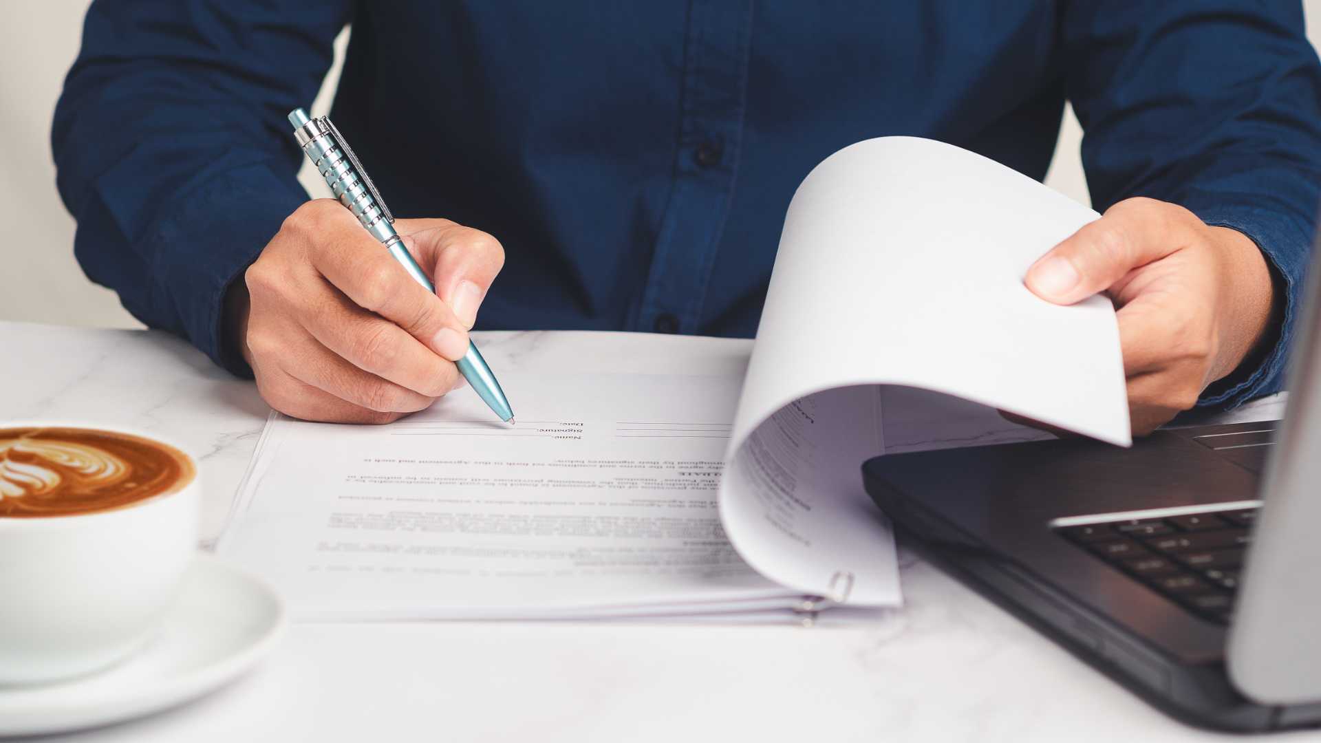 A person signs a contract with a pen while wearing a black shirt at a bright desk.