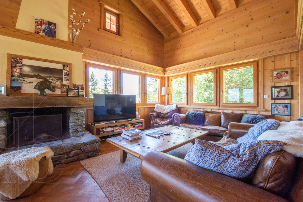 Salon chaleureux en bois avec cheminée et grandes fenêtres – Chalet Le Varouet  à vendre - Verbier