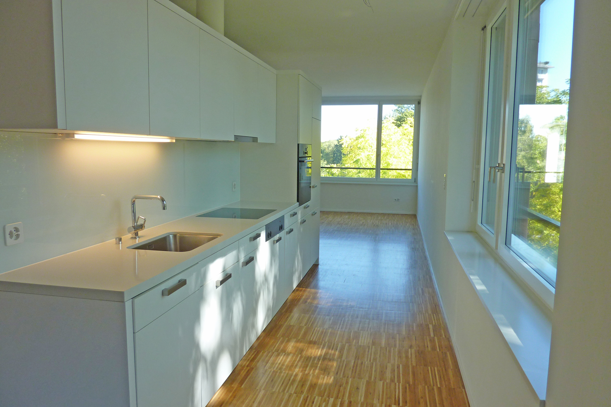 an empty kitchen with white cabinets and a large window and wooden floors