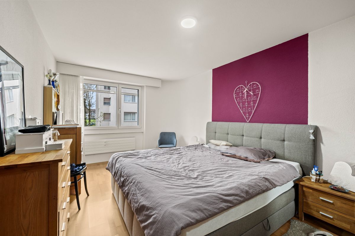 Helles Schlafzimmer mit großem Fenster und farbigem Akzent.