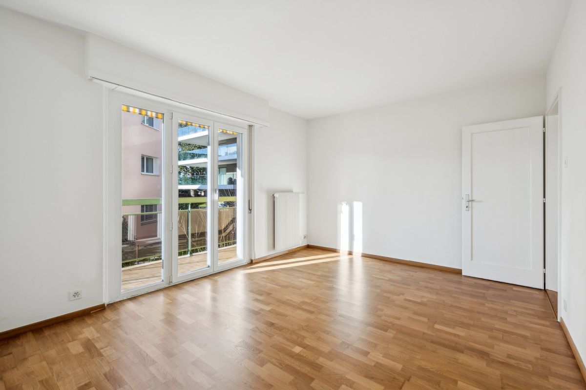 Salon avec parquet donnant sur un balcon par une grande porte-fenêtre.