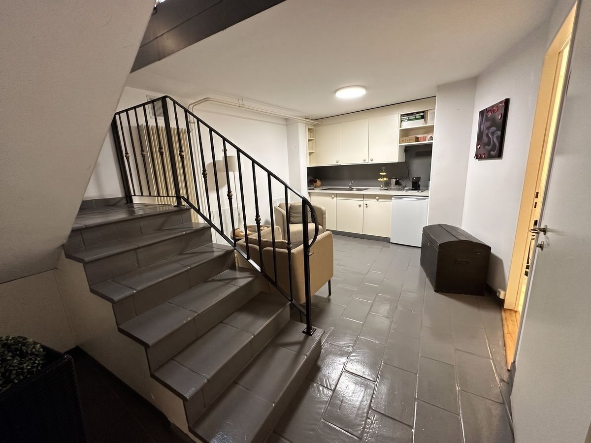 Espace avec kitchenette et coin salon, près d'un escalier.