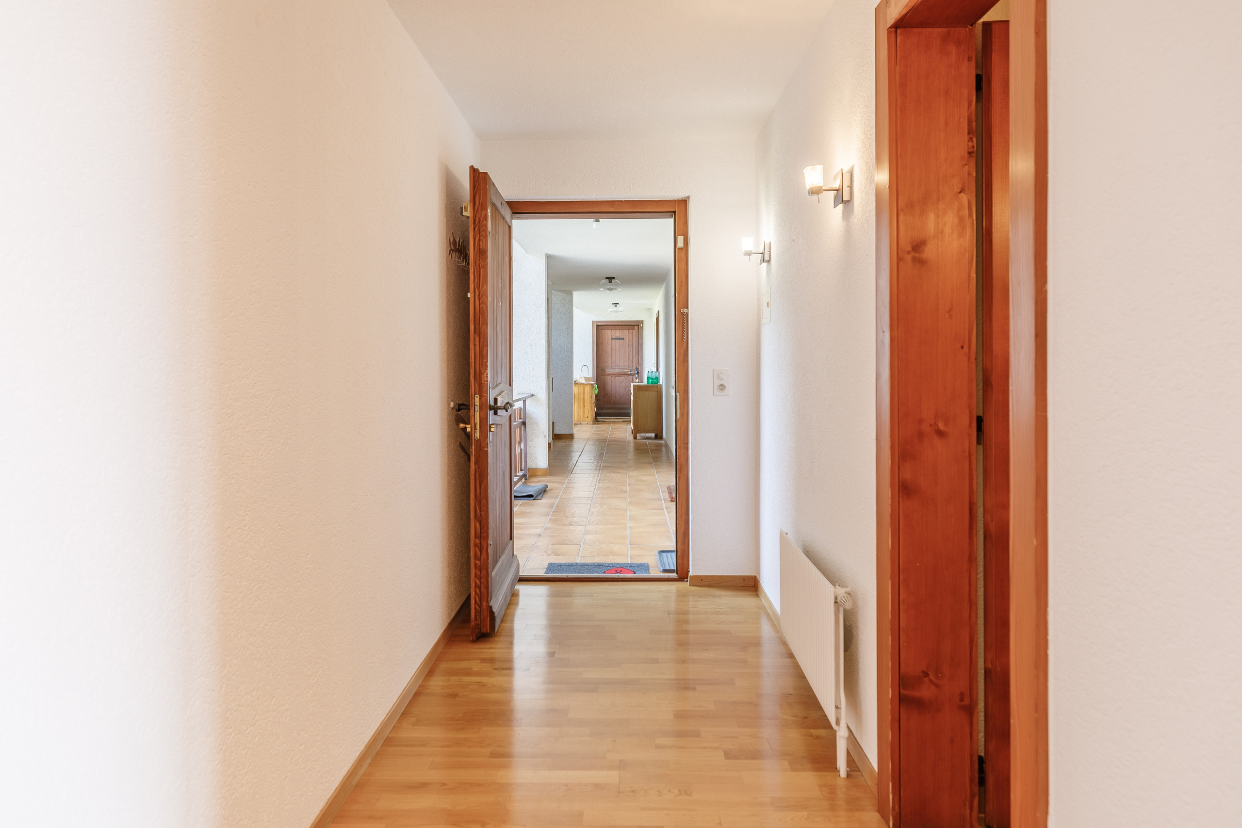 un long couloir avec des sols en bois et des murs blancs et une porte en bois qui mène à une autre pièce de la maison un long couloir avec des sols en bois et des murs blancs et une porte en bois qui mène à une autre pièce de la maison