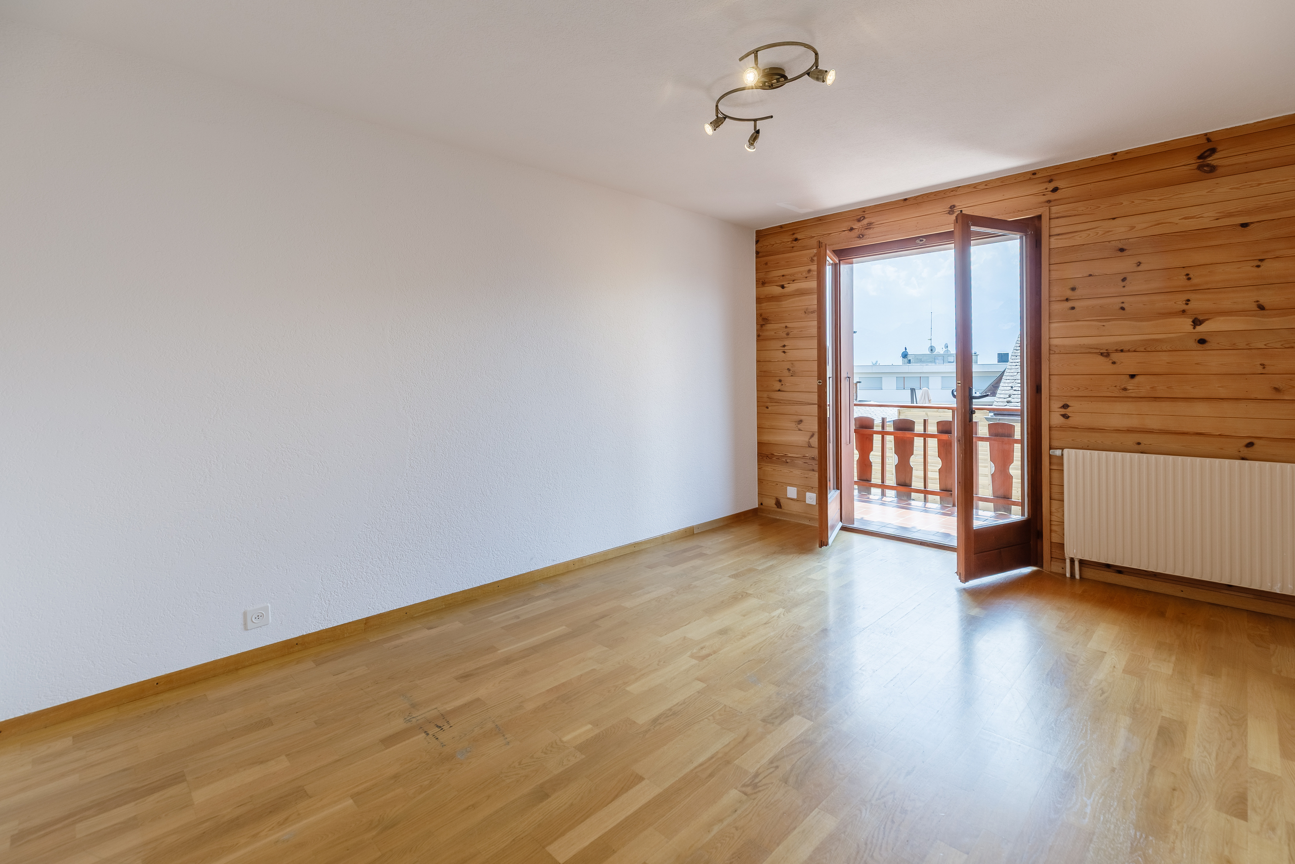 une pièce vide avec du parquet, une grande fenêtre et une porte qui mène à un balcon