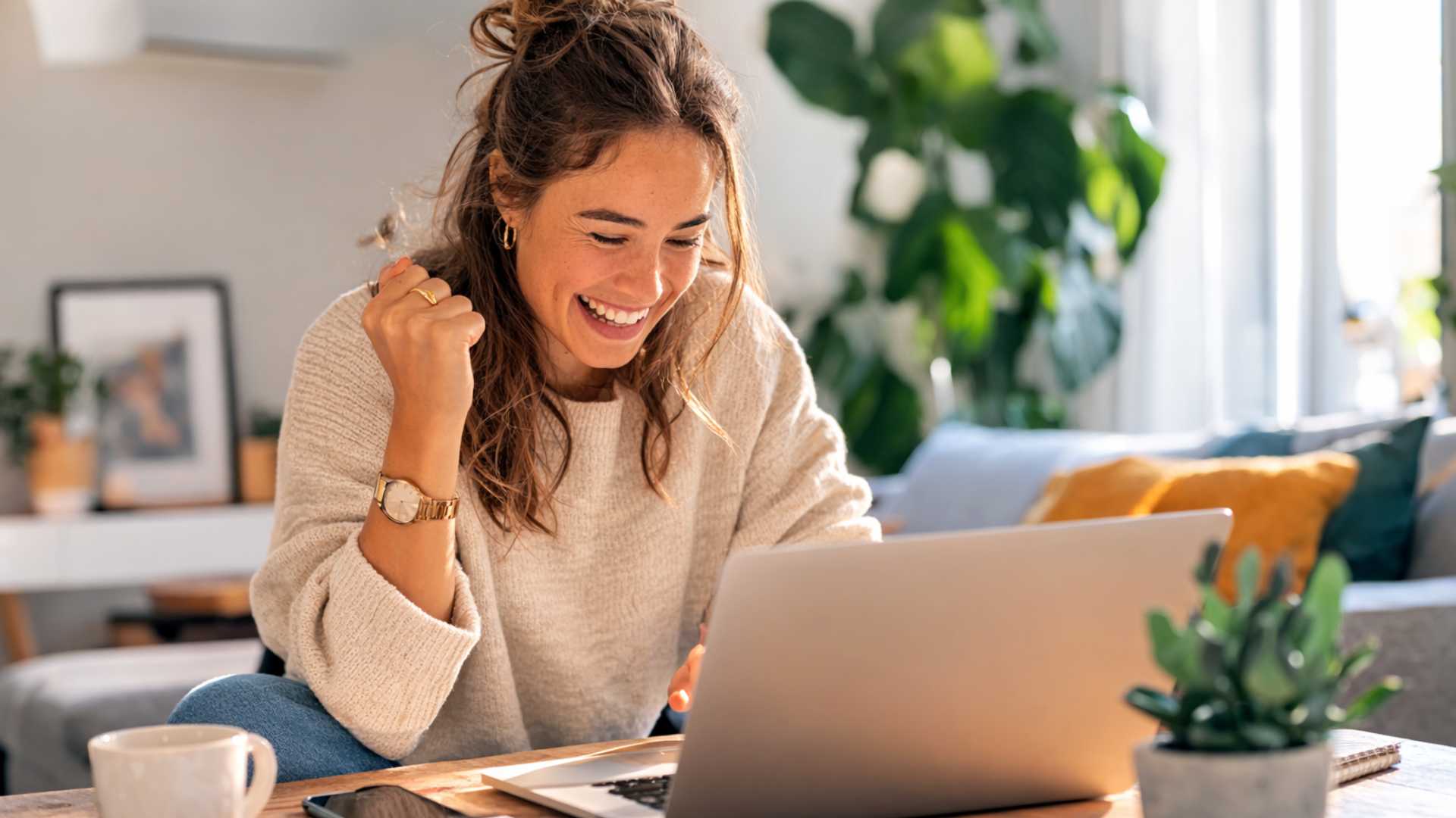 Jeune femme souriante assise à un bureau avec un ordinateur portable et un dossier de documents, heureuse de préparer sa candidature pour louer un appartement.