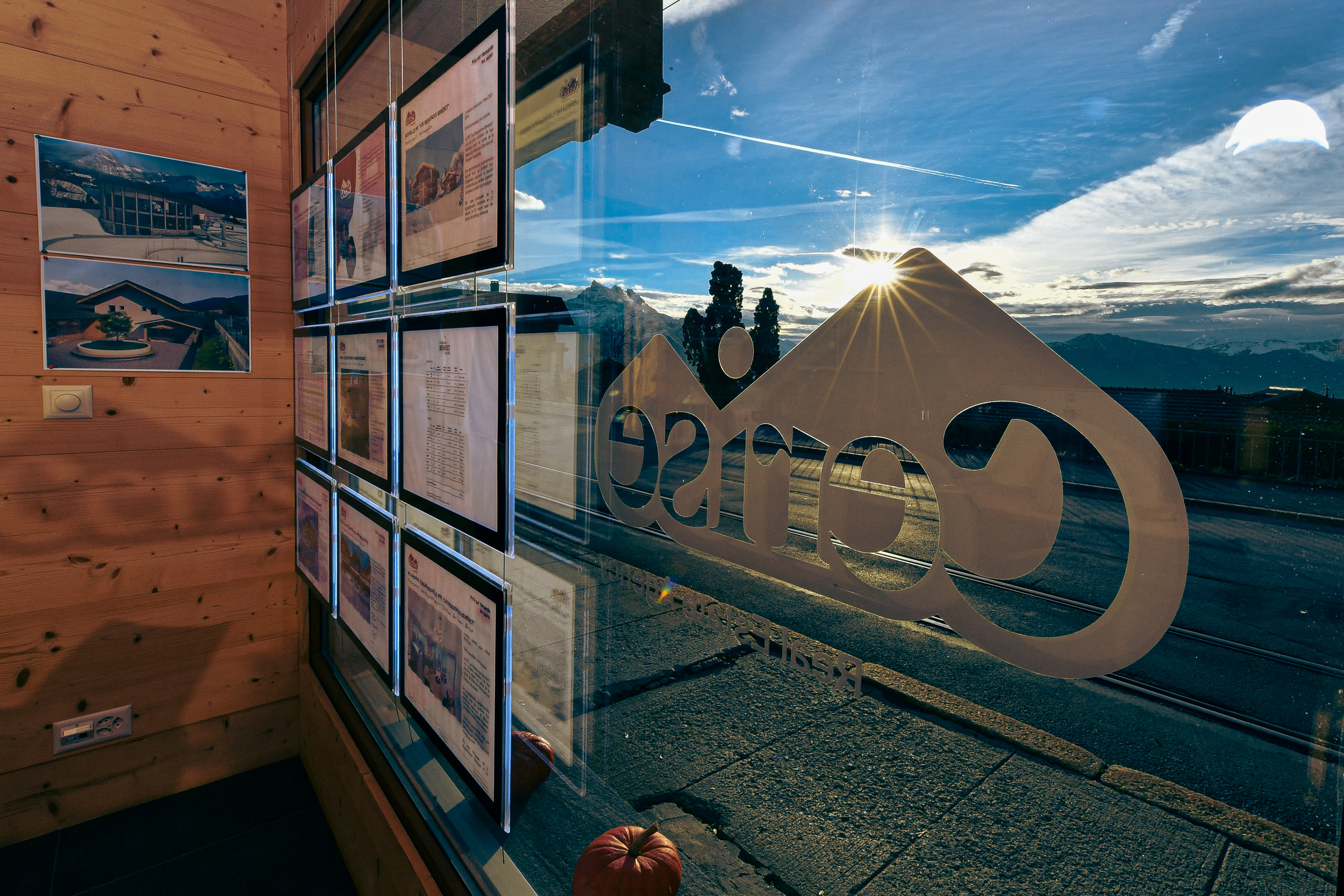 The Cerise Immobilier window illuminated by the last rays of the sun, offering a view of real estate advertisements in Switzerland. The dusk light brings a warm ambiance and highlights the agency's commitment to showcasing local real estate opportunities.