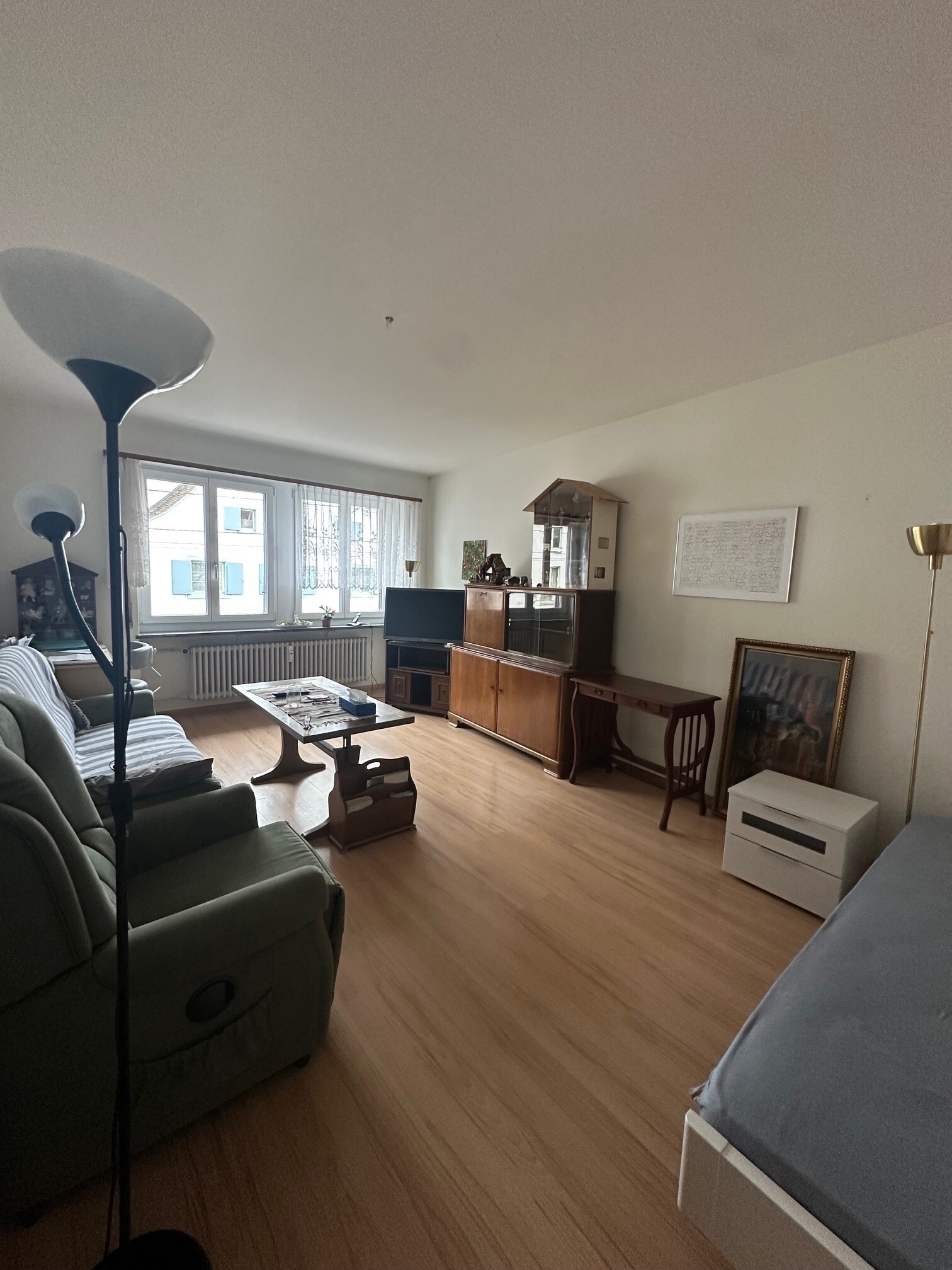 a room with a large window, a wooden floor, a couch, a table and chairs