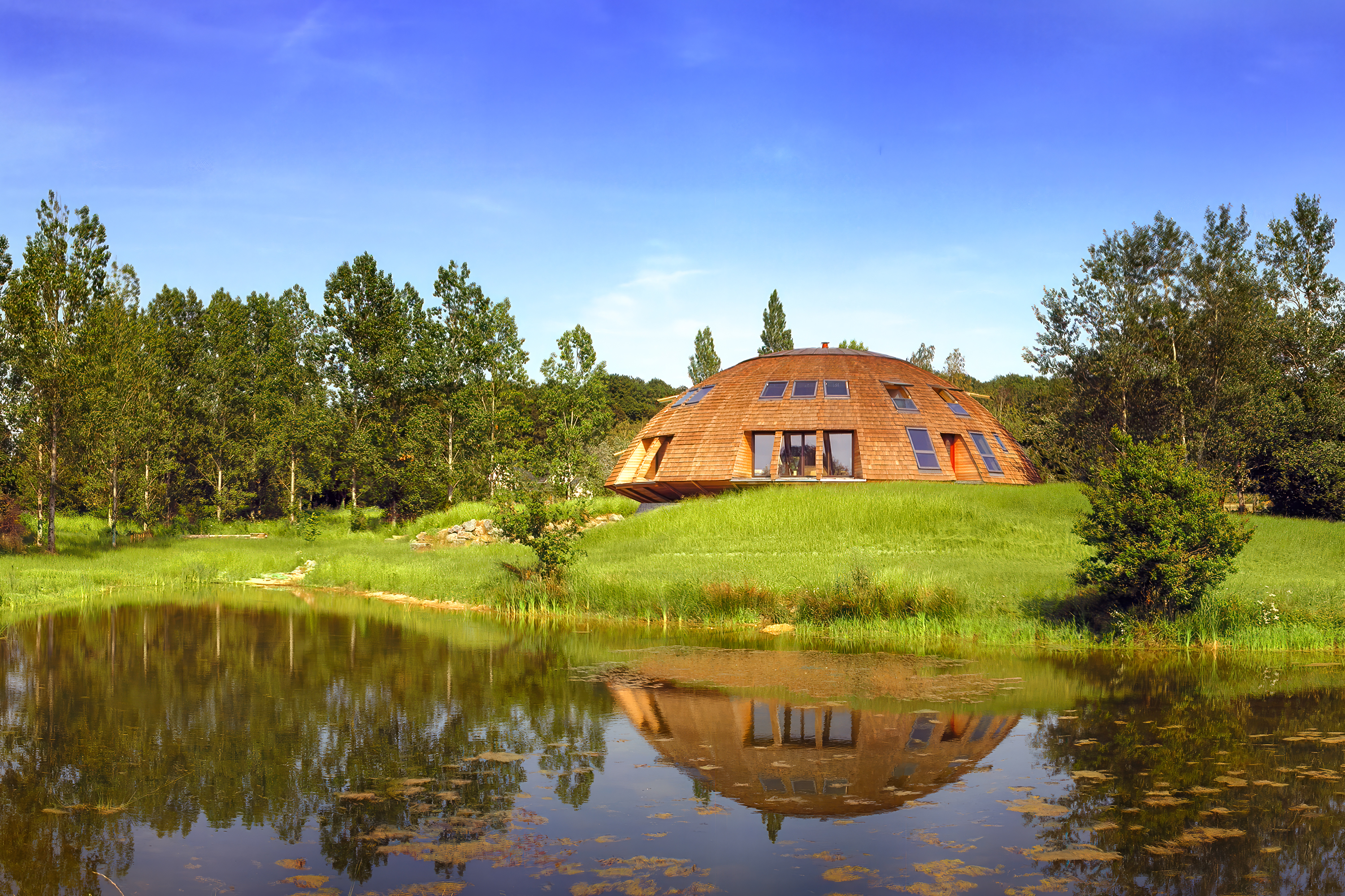Maison écologique Domespace en bois entouré de forêt au bord d'un étang.