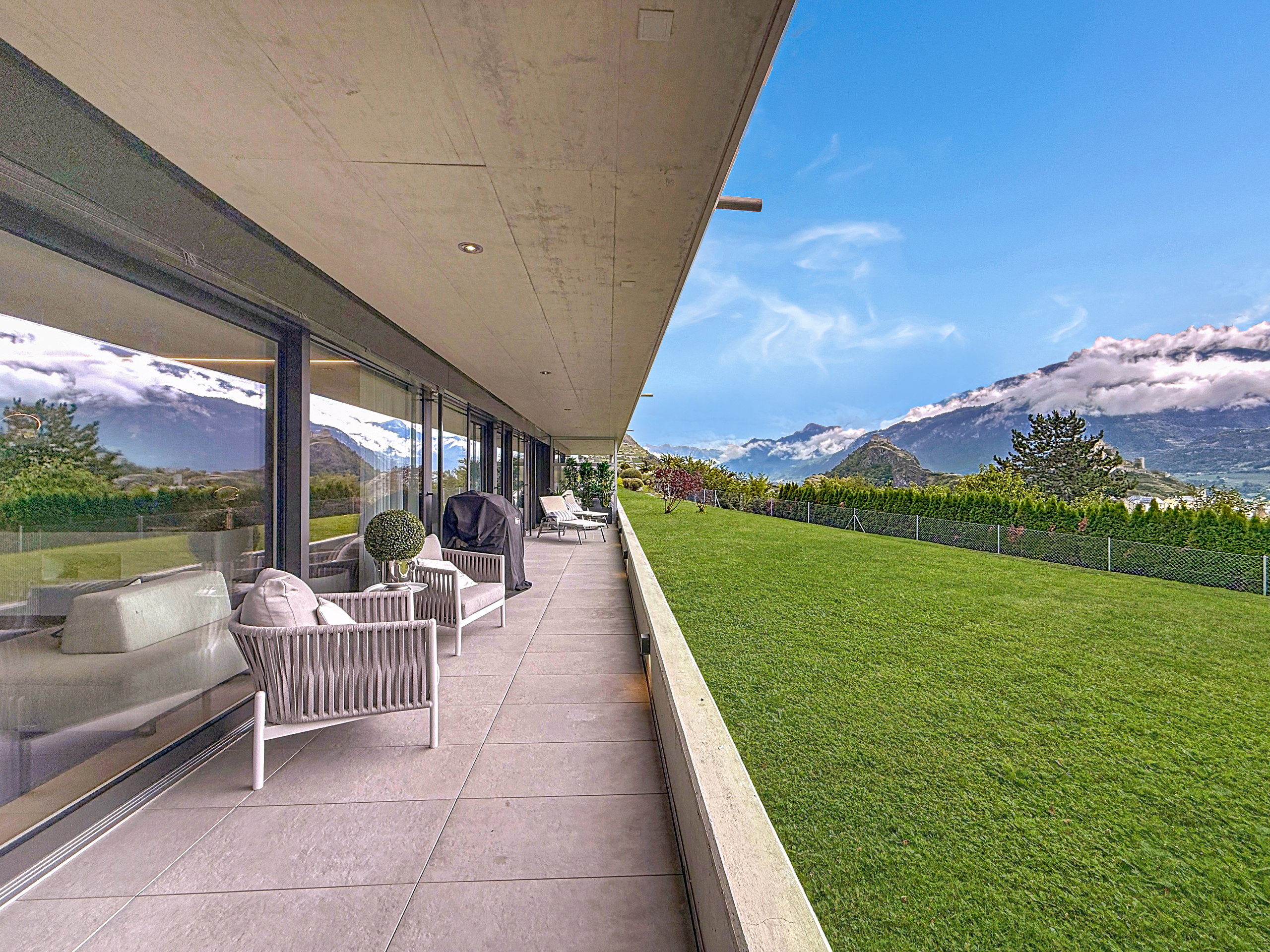 a balcony or patio with large windows overlooking green grass and mountains a balcony or patio with large windows overlooking green grass and mountains
