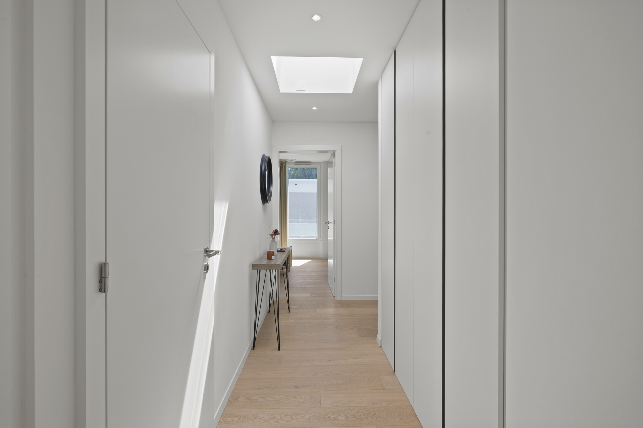 a long narrow hallway with white walls and floors and a skylight above the door that leads to another room in the house a long narrow hallway with white walls and floors and a skylight above the door that leads to another room in the house