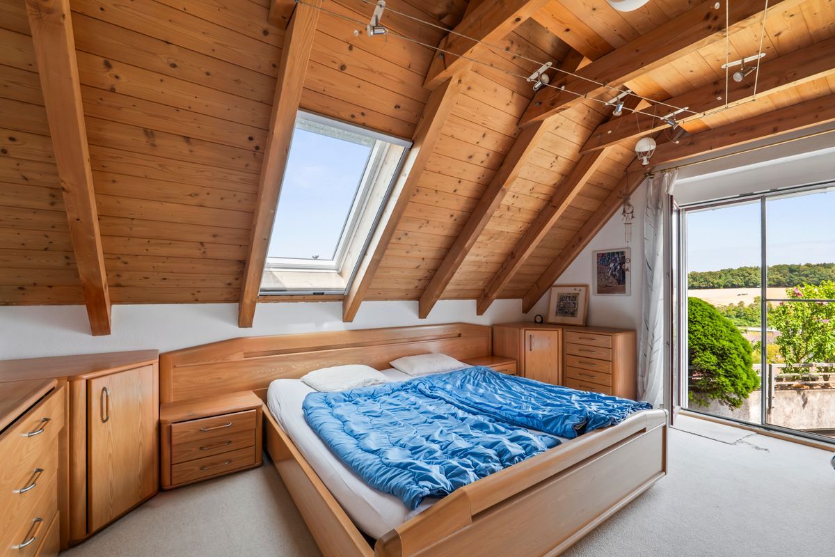 Dachzimmer mit Holzbalkendecke und großem Fenster.