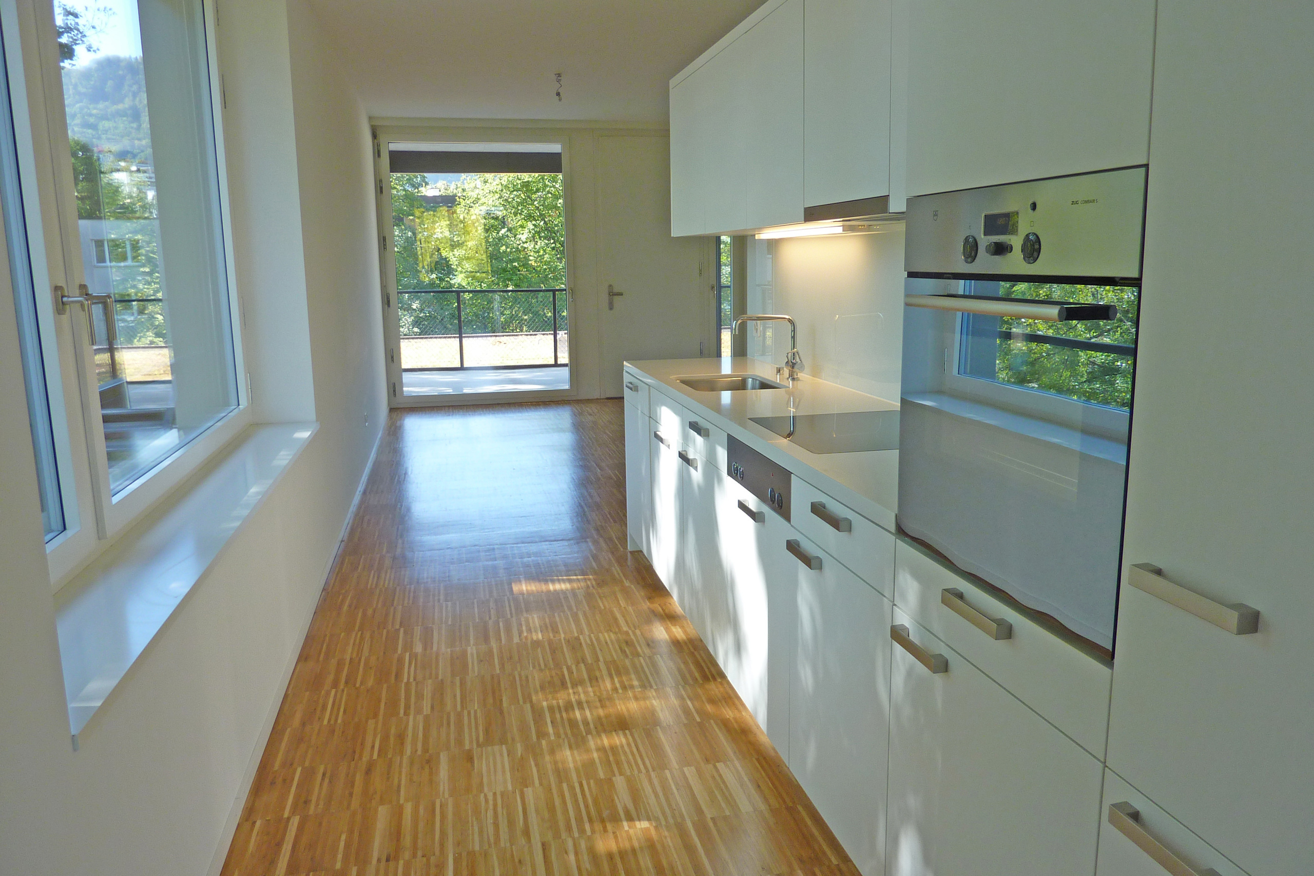 a long hallway in a modern house with white cabinets and a large window and a long wooden floor