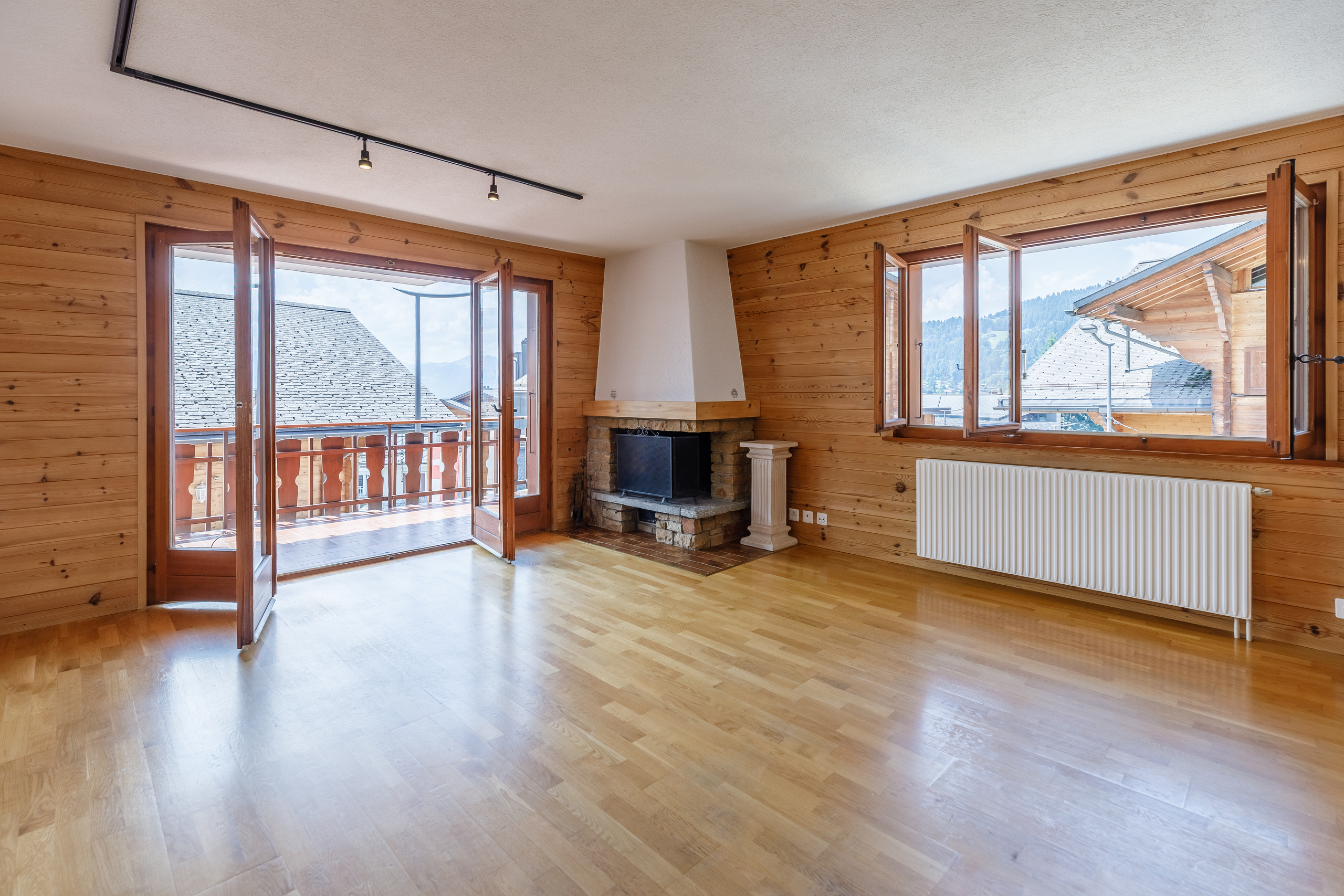 un salon avec parquet, cheminée et grandes fenêtres