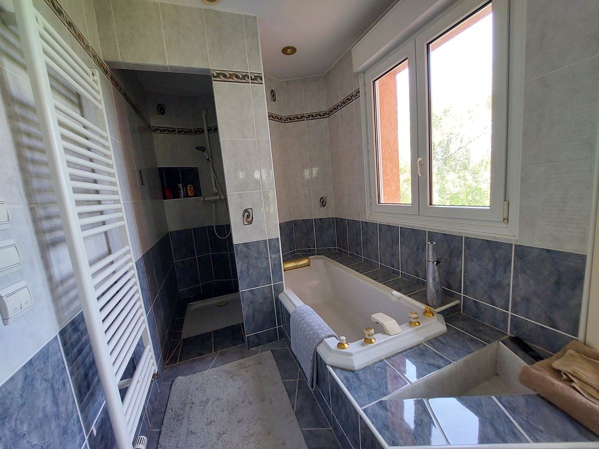 Salle de bain avec baignoire, douche et fenêtre lumineuse.