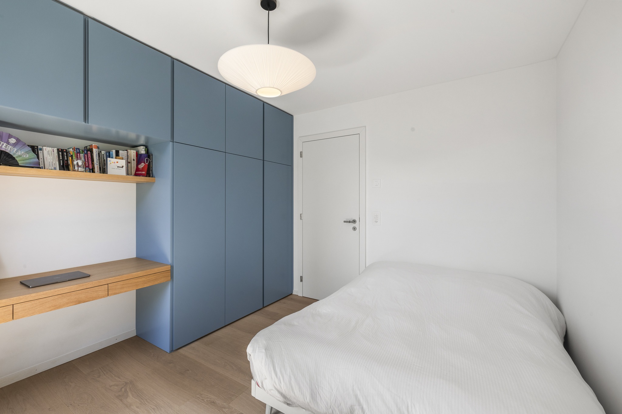 a small bedroom in an apartment with a white wall, blue cabinets and a bed a small bedroom in an apartment with a white wall, blue cabinets and a bed