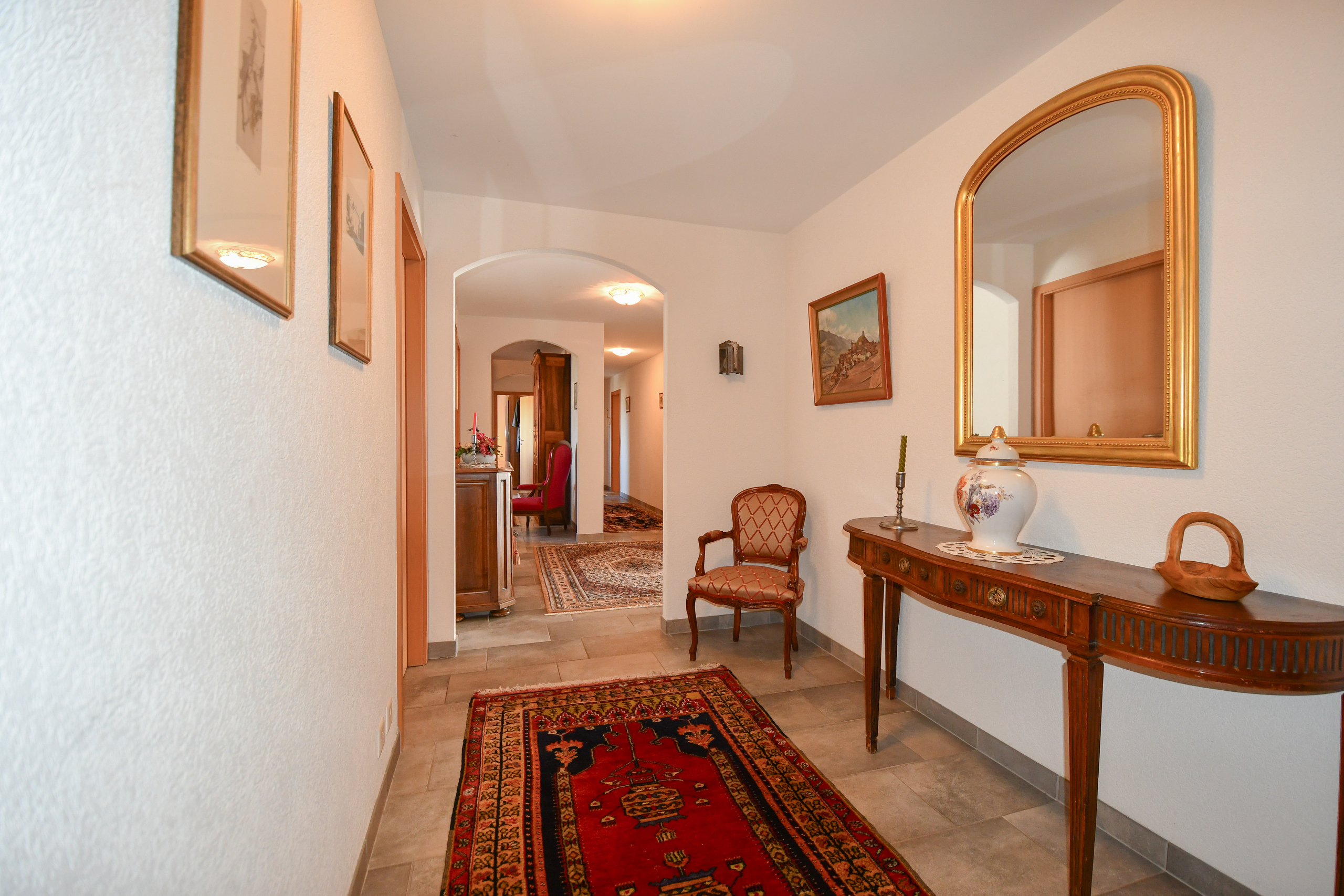 a hallway of a home with a chair, table, mirror and rug on the floor