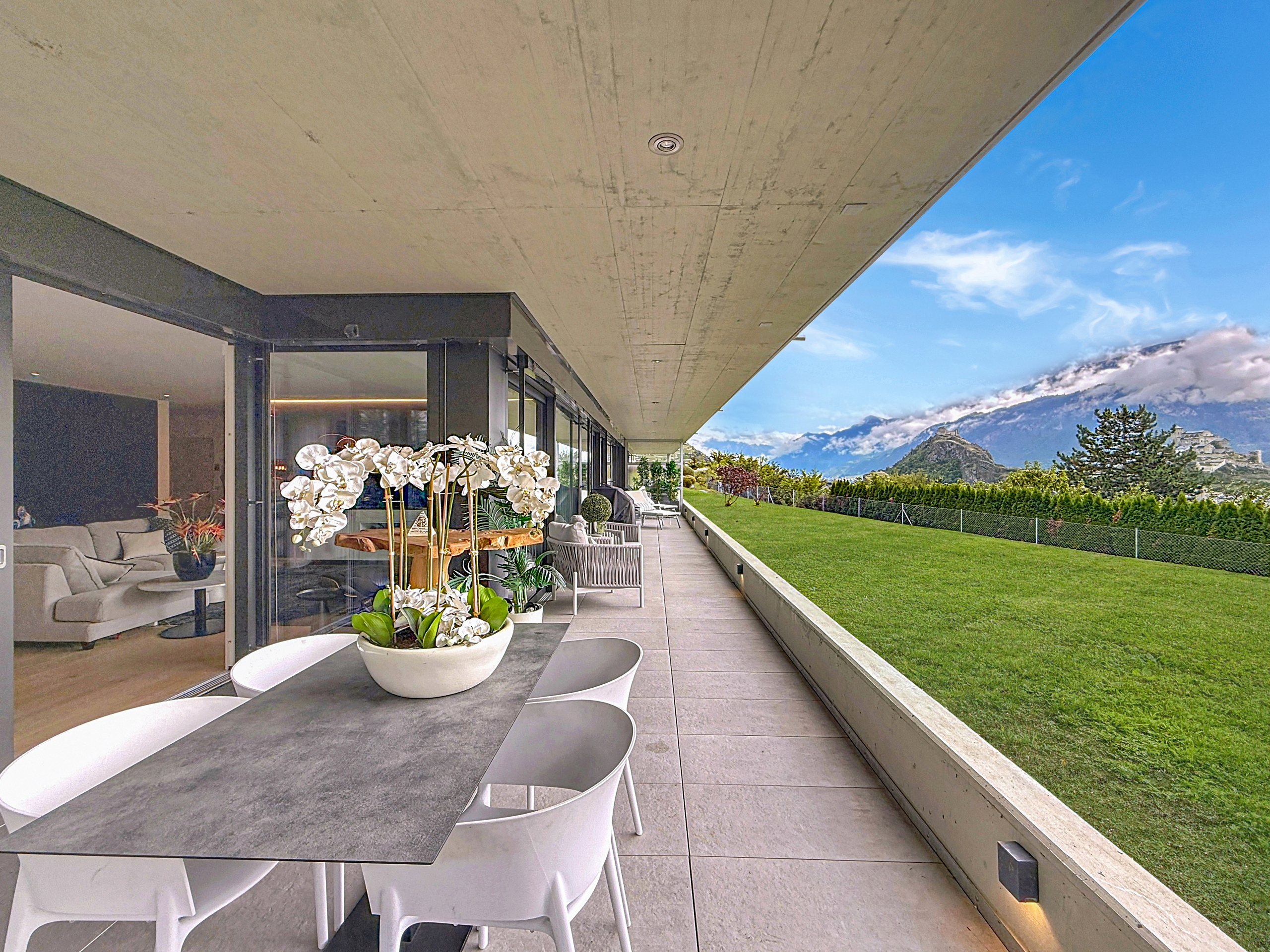 a large balcony with a dining table and chairs overlooks the mountains from a modern home a large balcony with a dining table and chairs overlooks the mountains from a modern home