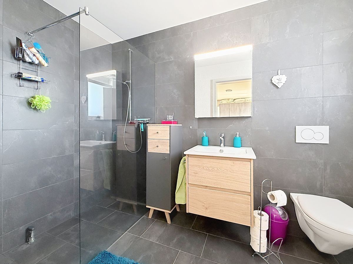 Salle de bain avec douche moderne et lavabo suspendu.