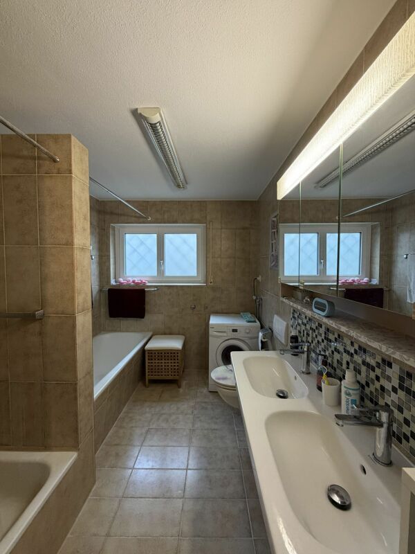 Badezimmer mit Badewanne, Dusche, Doppel-Lavabo, Waschmaschine und Fenster
