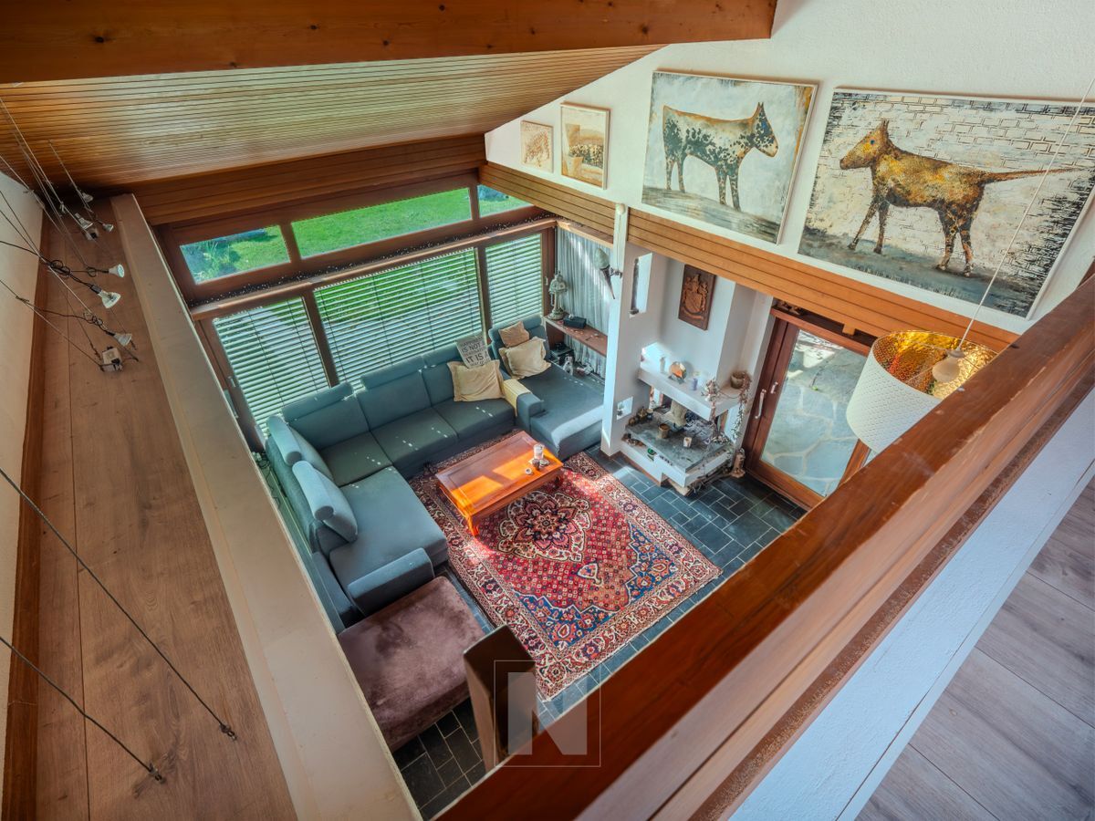 Vue aérienne du salon mettant en valeur sa belle hauteur sous plafond, sa cheminée et son ambiance chaleureuse et cosy.
