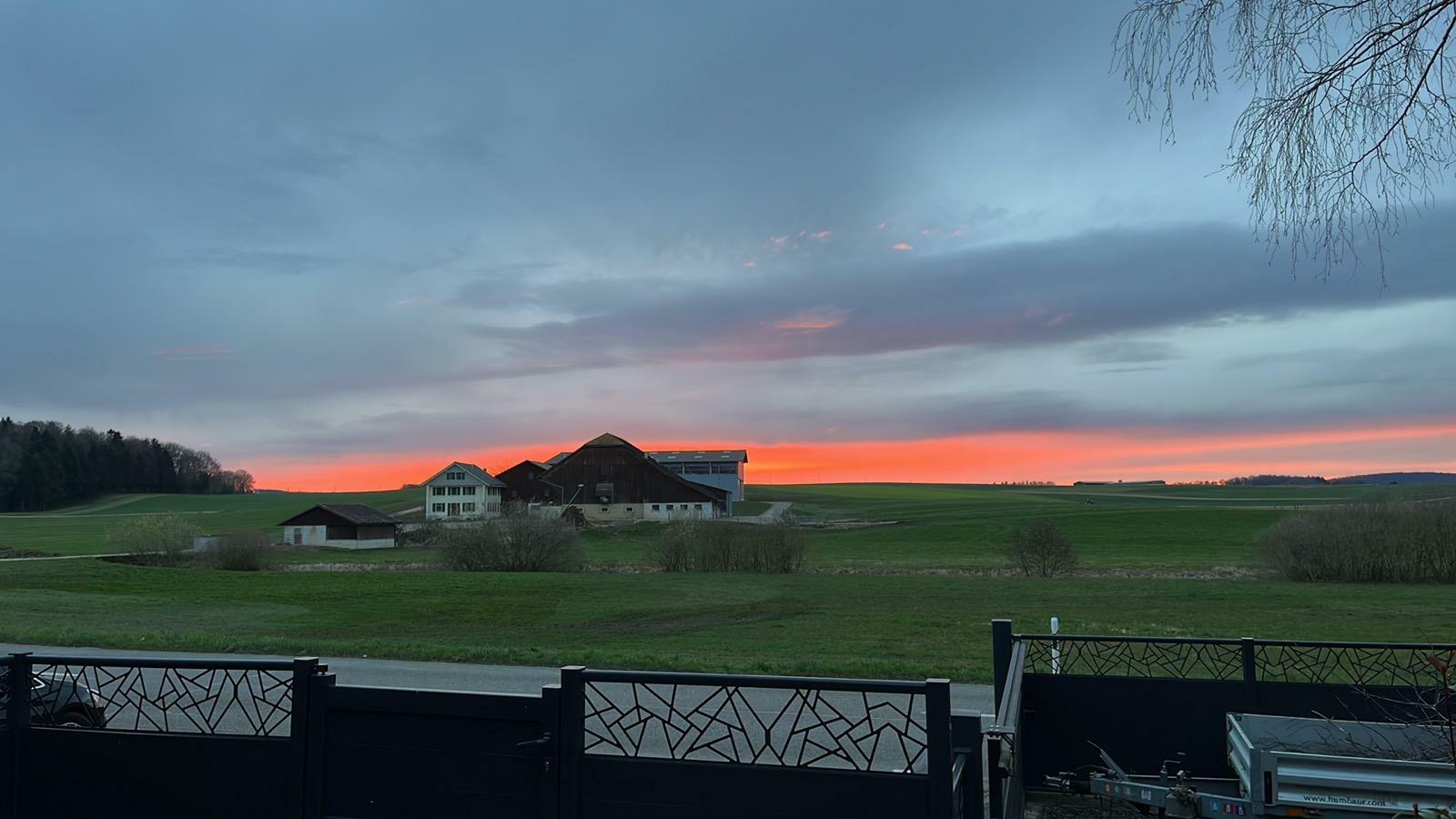 un beau coucher de soleil sur une ferme avec une maison au premier plan