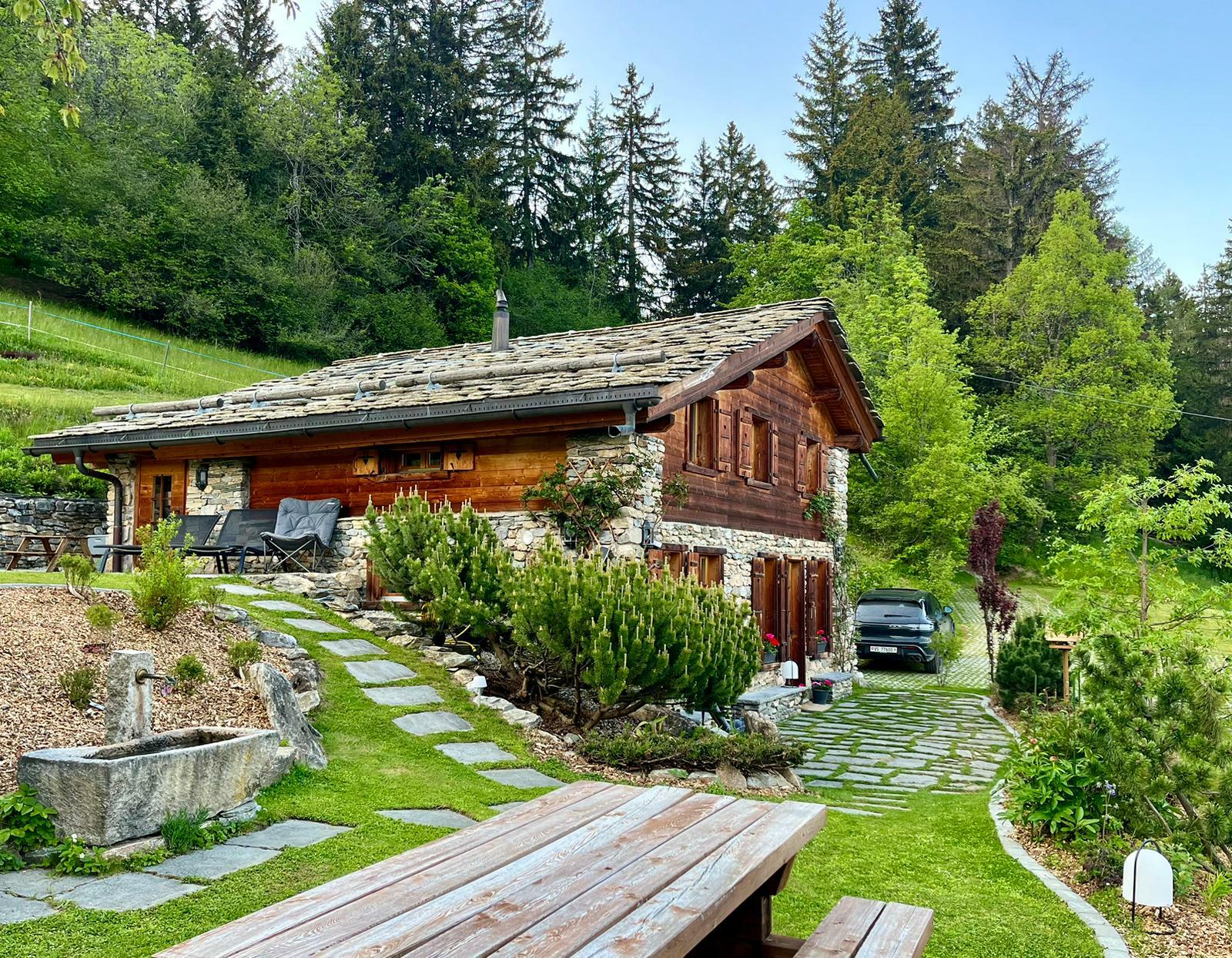 a wooden bench and picnic table in front of a small house in a garden
