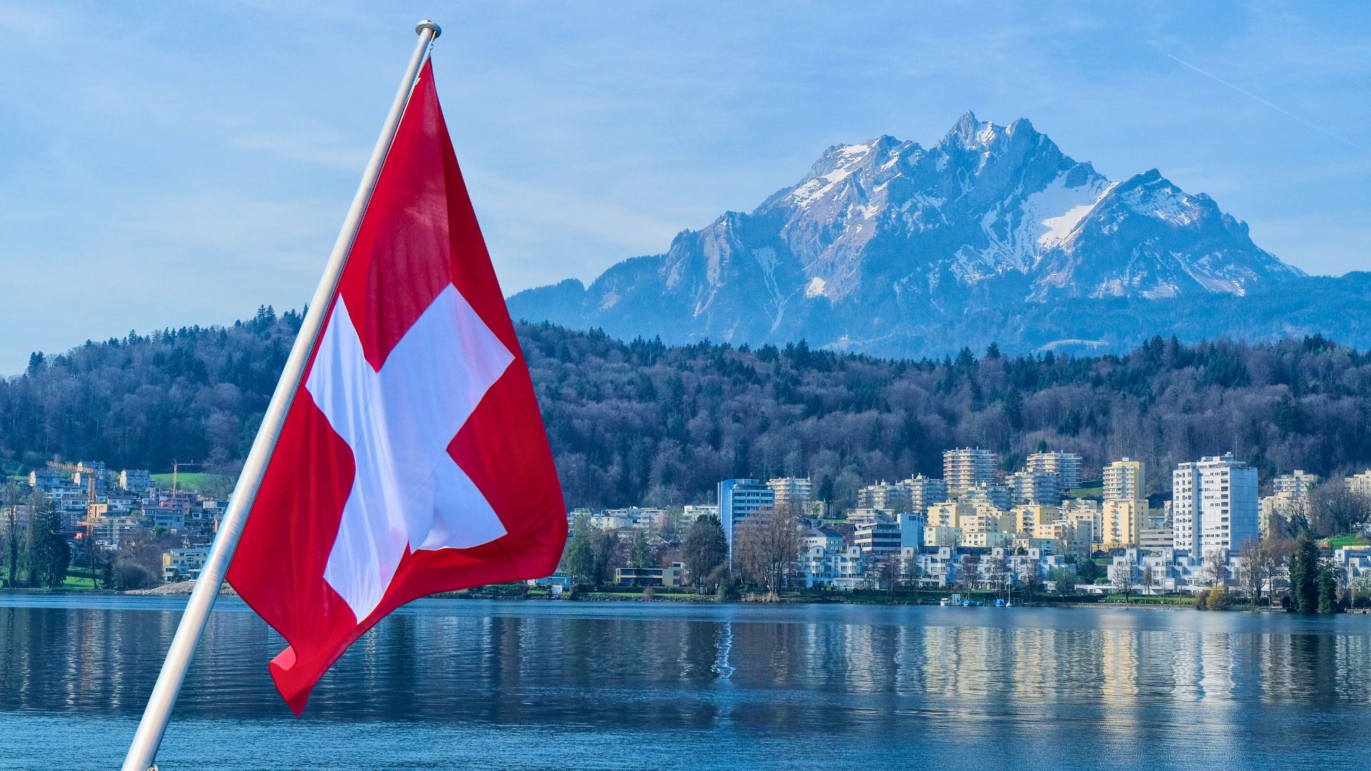 Drapeau suisse devant un paysage urbain et montagneux, symbolisant les enjeux du marché immobilier suisse, de la croissance démographique et de la votation sur l’initiative « Suisse à 10 millions ».