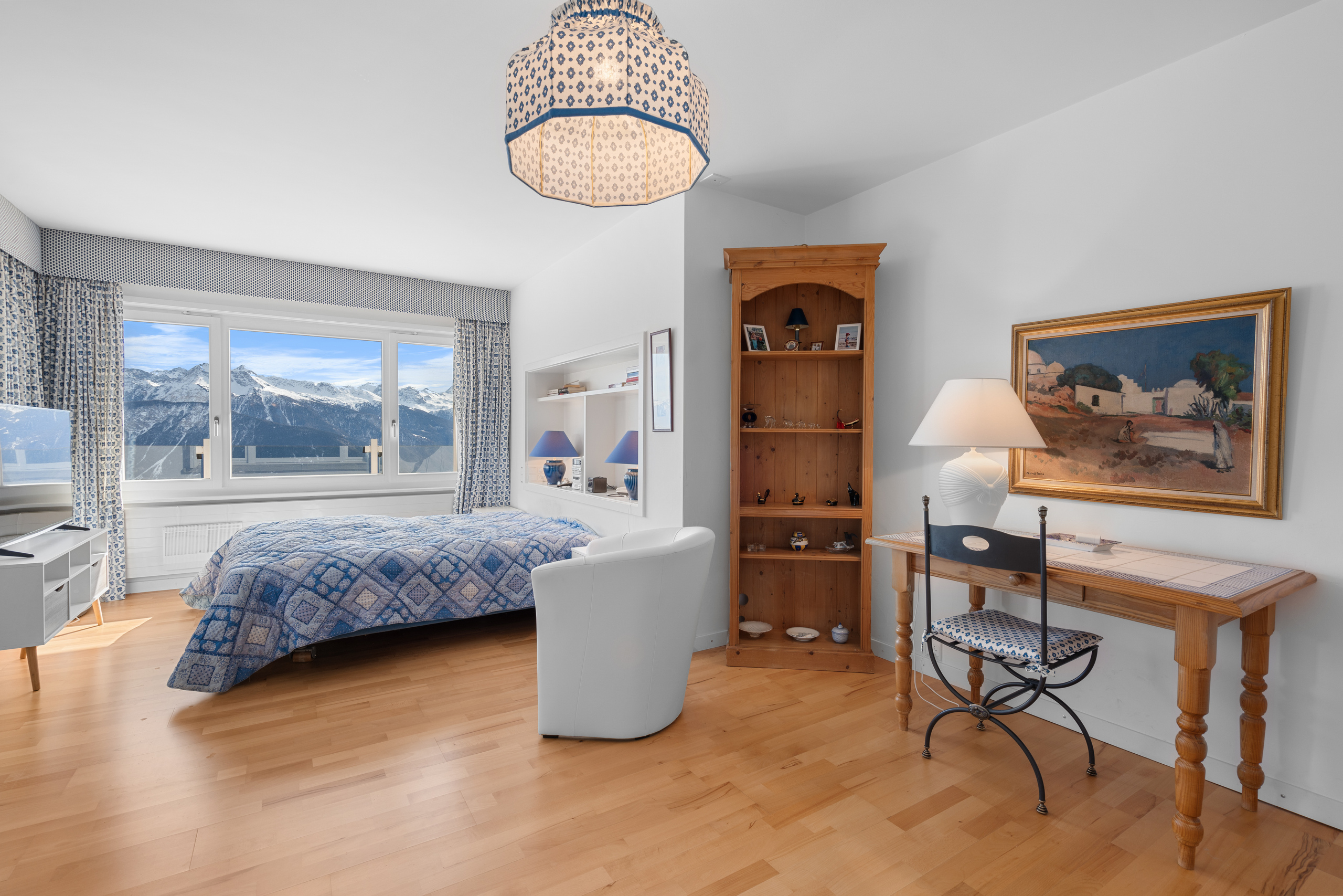 une chambre avec du parquet, une grande fenêtre, un lit et un bureau