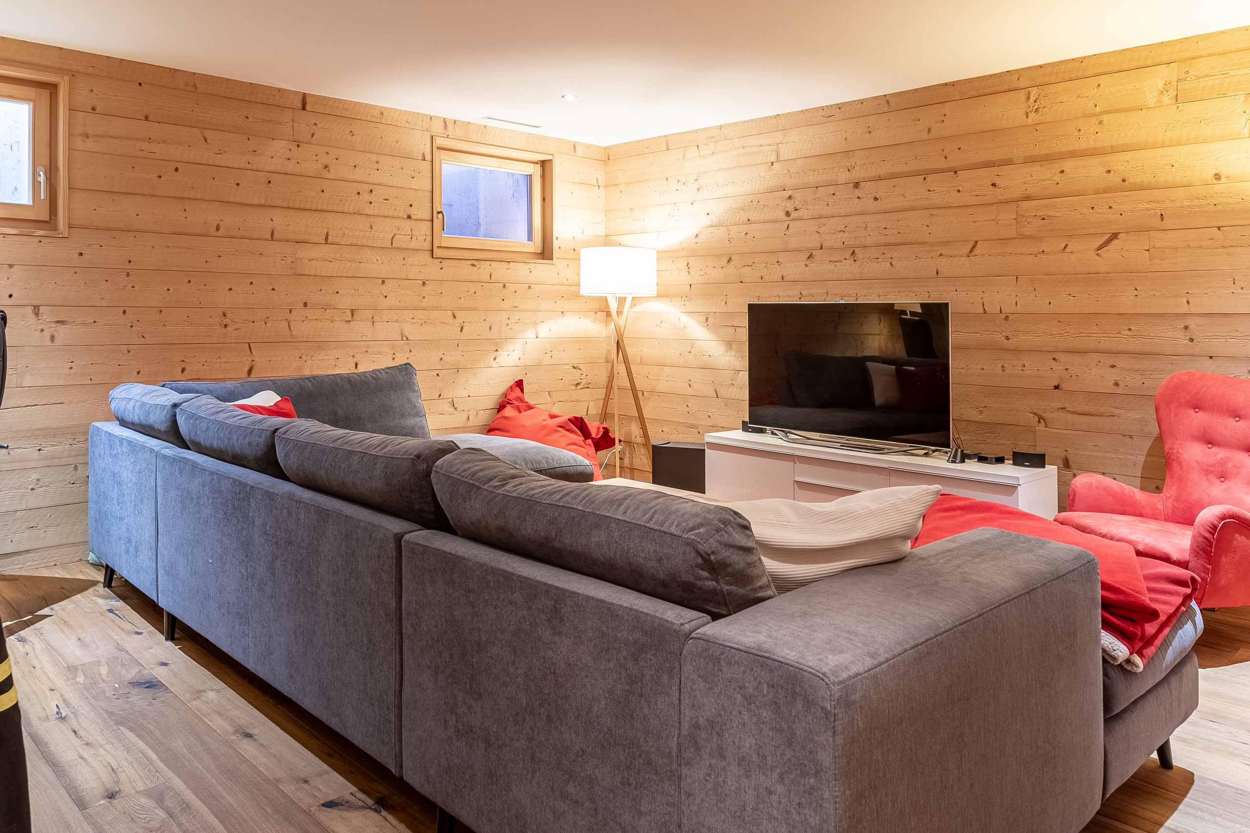 un salon avec des murs en bois, un grand canapé, une chaise, une cheminée et une télévision un salon avec des murs en bois, un grand canapé, une chaise, une cheminée et une télévision