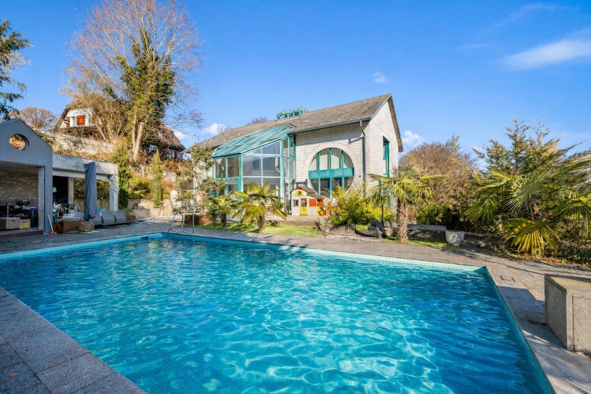 Grosszügiger Aussenpool vor moderner Villa mit grossen Glasfronten, eingebettet in einen gepflegten Garten mit Palmen und sonniger Terrasse Grosszügiger Aussenpool vor moderner Villa mit grossen Glasfronten, eingebettet in einen gepflegten Garten mit Palmen und sonniger Terrasse