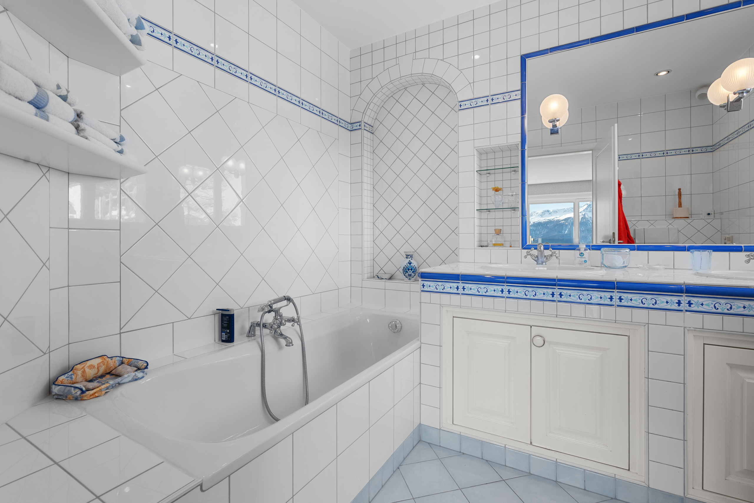 une salle de bains avec des carreaux blancs et bleus et un grand miroir au mur