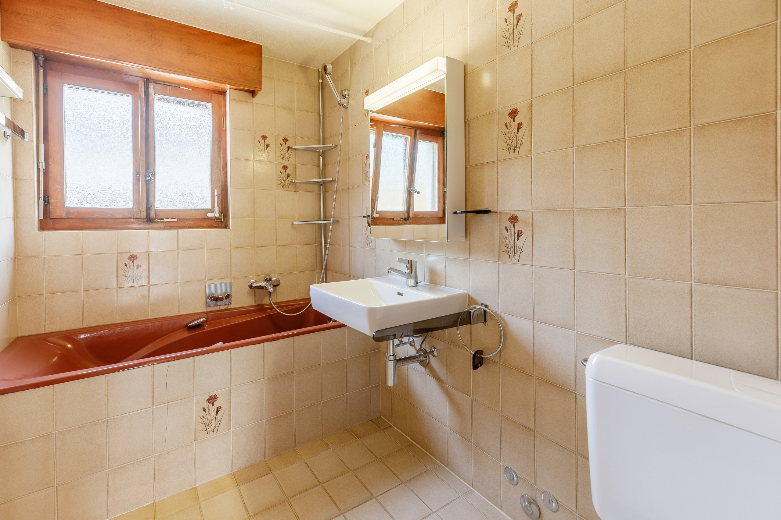 une salle de bains avec des carreaux blancs sur les murs, une baignoire rouge, un lavabo et un miroir