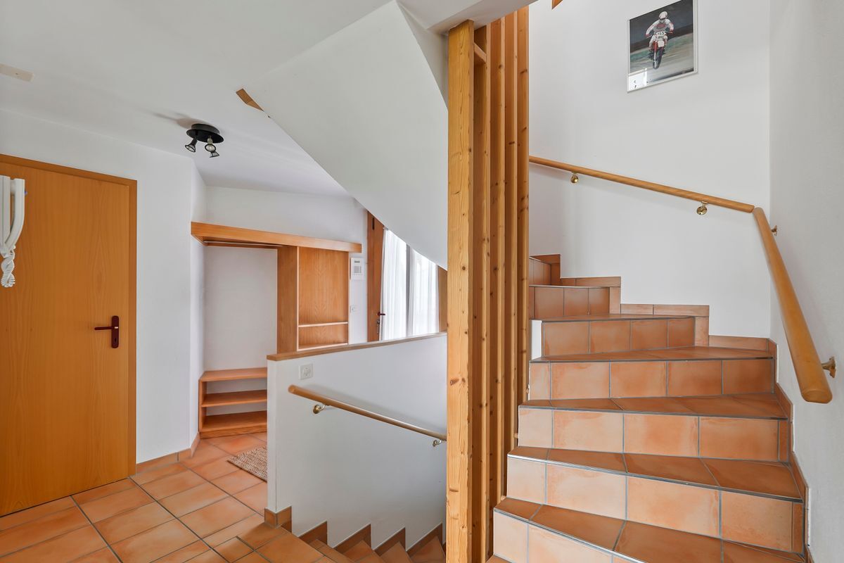Holztreppe mit Keramikfliesen-Boden in hellem Flur.