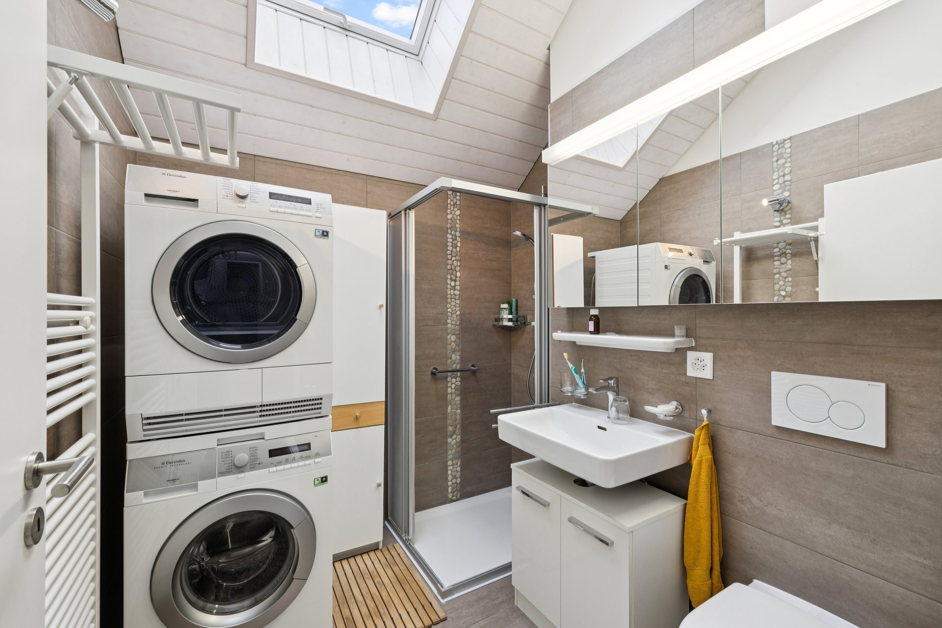 une salle de bains moderne avec toilettes blanches, lavabo, douche et machine à laver dans un petit grenier